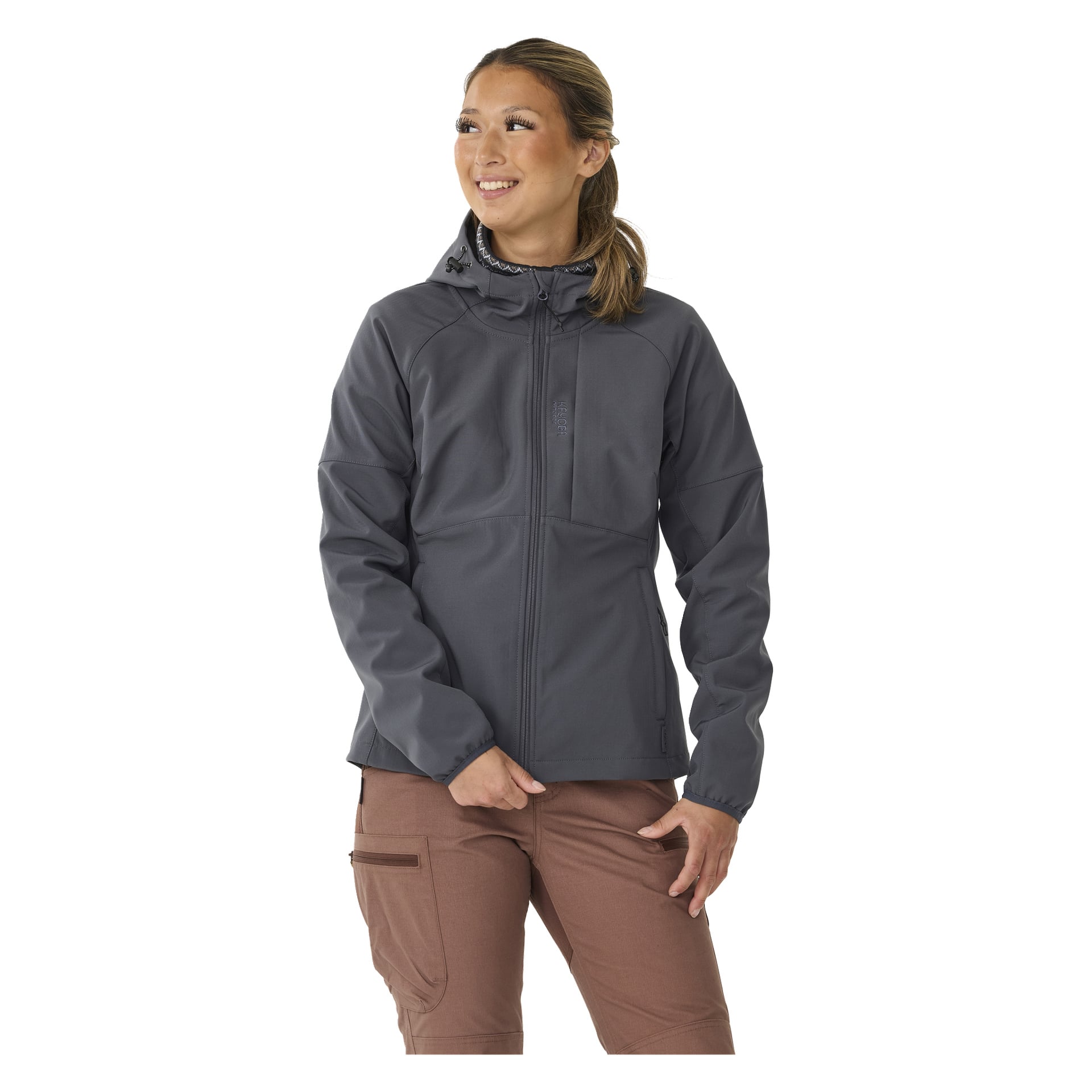 Eine Frau präsentiert die graue Kayoba Outdoor Women's Hede, fleecegefütterte Softshelljacke, die einen Reißverschluss vorne und Reißverschlusstaschen enthält. Sie kombiniert ihn mit brauner Hose, steht leicht schräg und lächelt.
