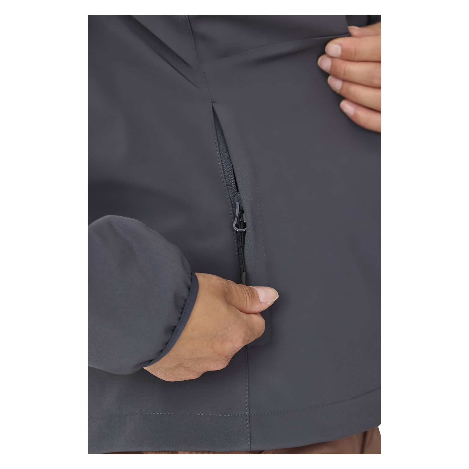Eine Hand ist zu sehen, wie sie eine Tasche am unteren Teil einer dunkelgrauen Kayoba Outdoor Women's Softshell-Softshelljacke Hede mit Fleece gefüttert wird. Das Bild konzentriert sich ausschließlich auf die Hand, den glatten Stoff und den schwarzen Reißverschluss.