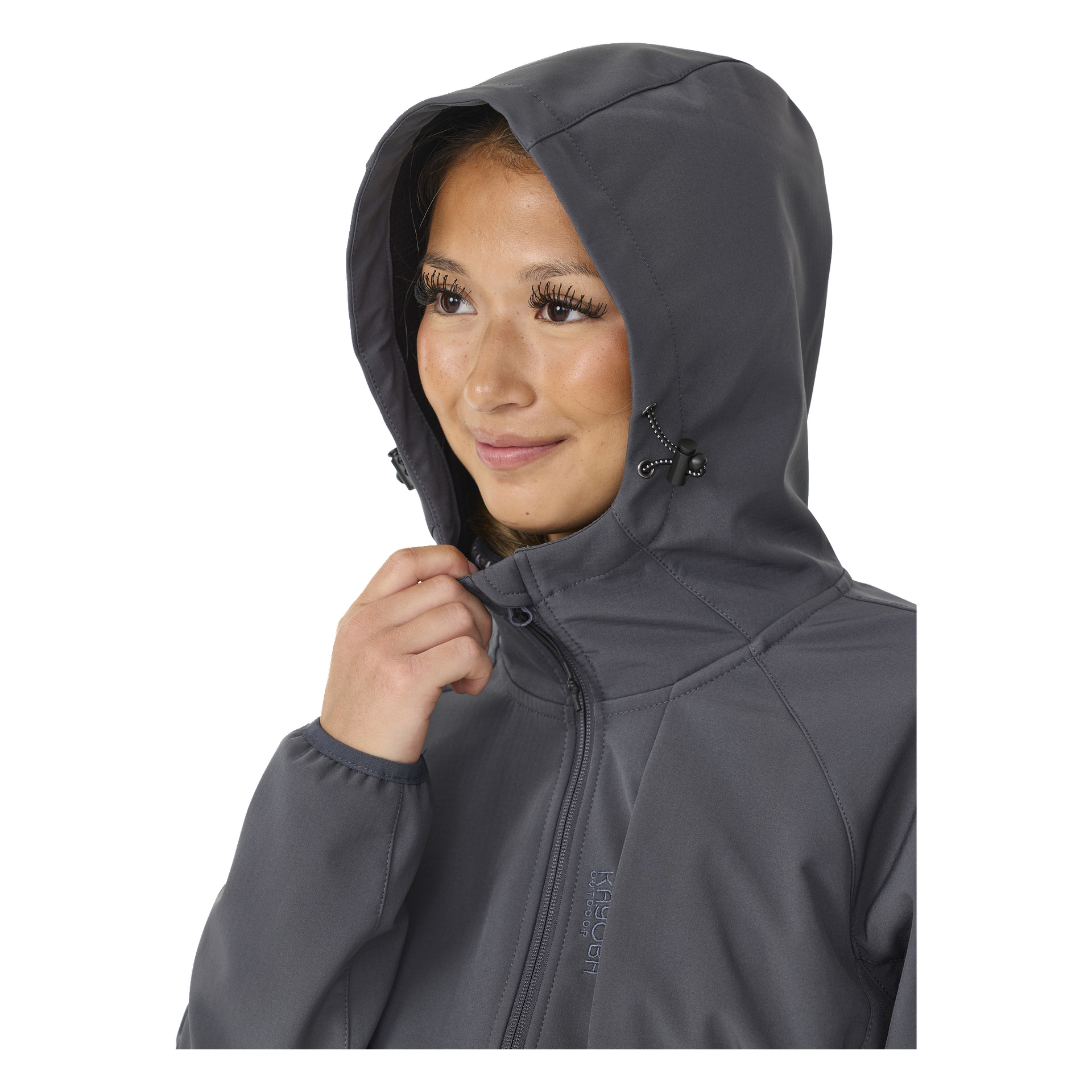 Eine Frau in einer dunkelgrauen, mit Fleece gefütterten Kayoba Outdoor Softshell-Jacke richtet mit einer Hand die Kapuze und blickt zur Seite. Die Jacke hat sichtbare Nahtdetails und Kordelverschlüsse an der Kapuze.