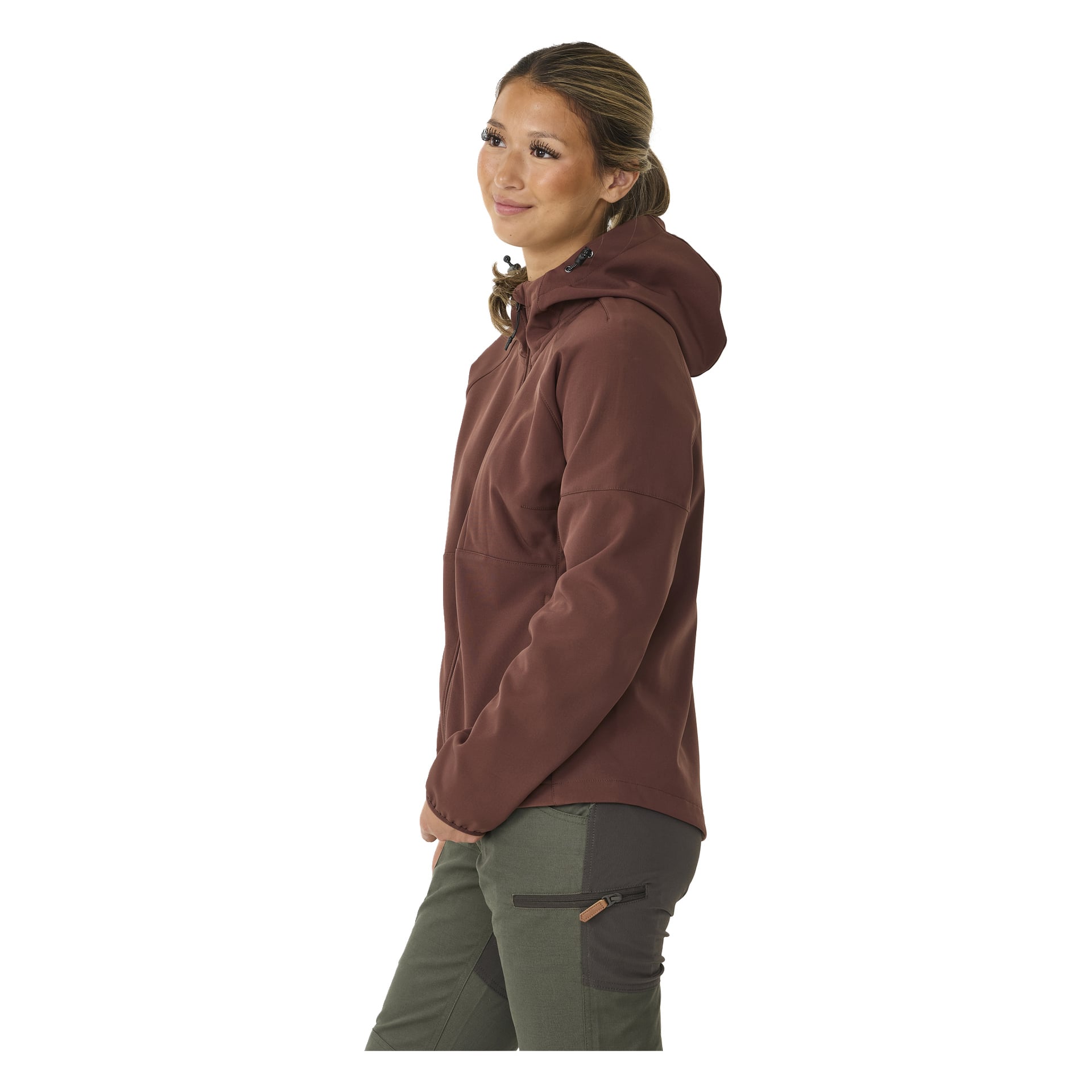 Eine Person mit langen Wimpern und zurückgebundenem Haar trägt die braune Kayoba Outdoor Women's Softshell-Jacke Hede, kombiniert mit zweifarbigen grünen Hosen mit Reißverschlusstaschen, steht auf und blickt leicht zur Seite.
