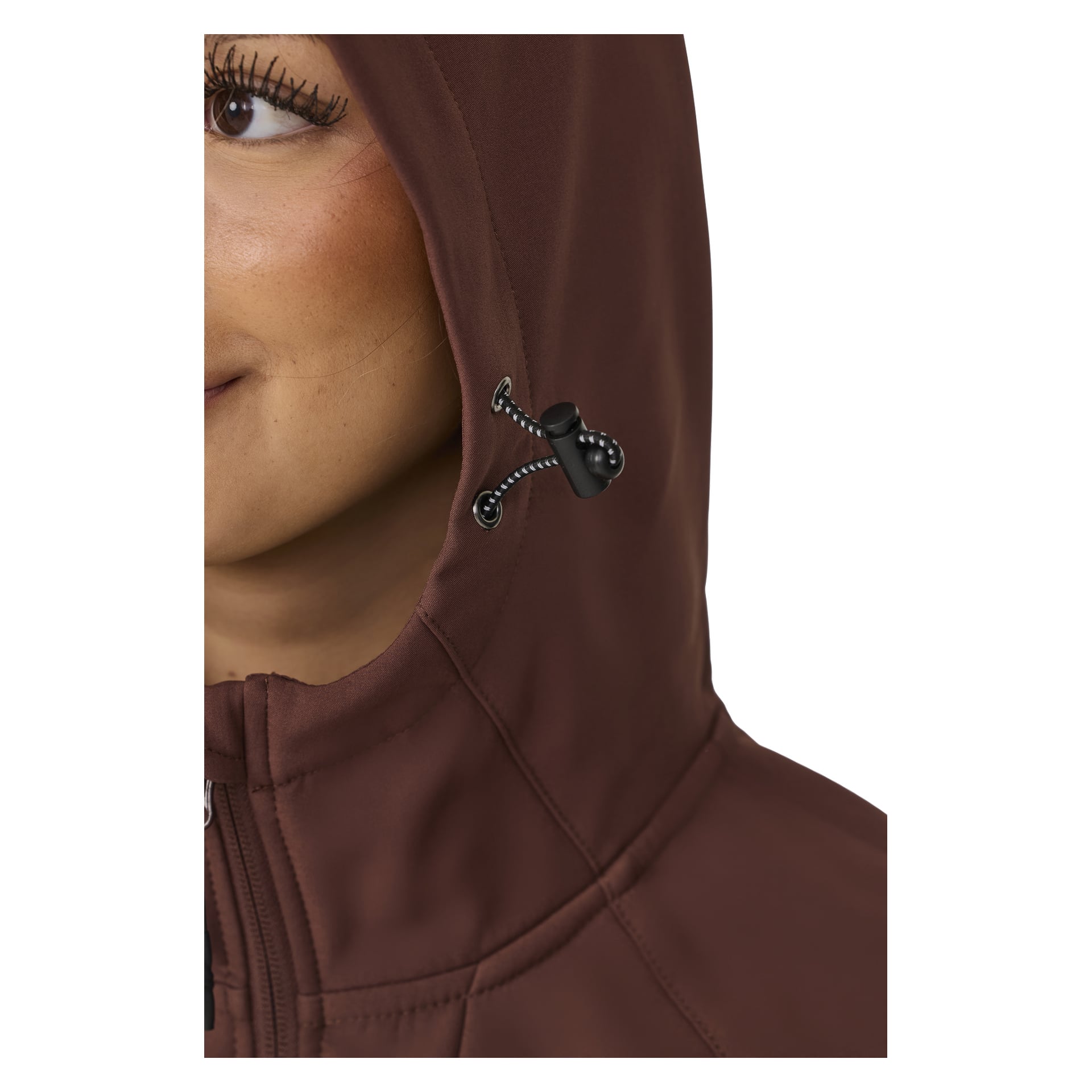 Nahaufnahme einer Person in der braunen, mit Fleece gefütterten Softshelljacke von Kayoba Outdoor Women, Hede, Kapuze mit schwarzem Kippzug festgezogen und Reißverschluss bis zum Kragen hochgezogen. Die linke Seite ihres Gesichts ist sichtbar.