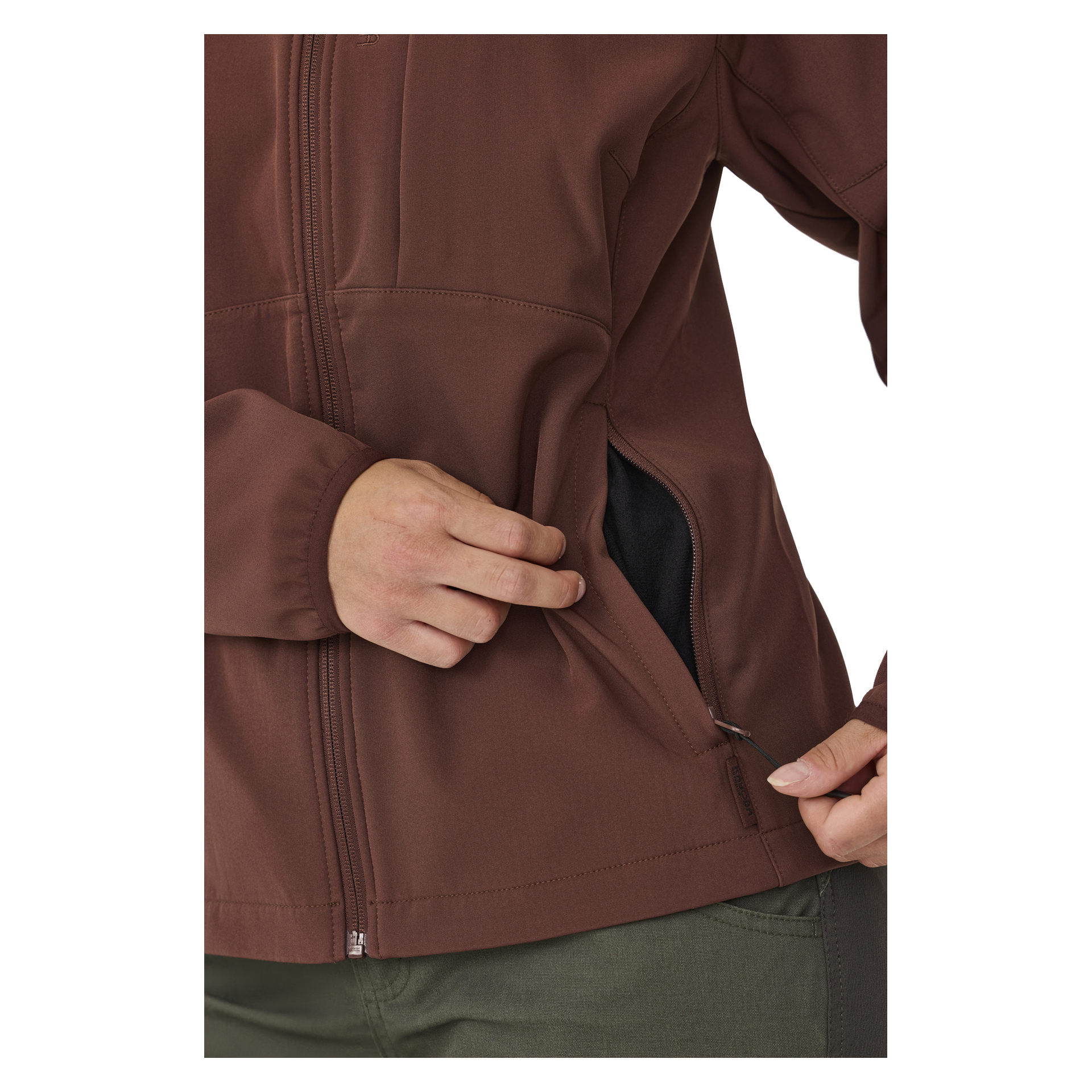 Jemand zeigt die braune Kayoba Outdoor Women's Softshell-Softshell-Jacke Hede, steckt die linke Hand in eine Seitentasche und greift mit der rechten Hand den Reißverschluss der Tasche. Sie tragen außerdem olivgrüne Hosen.