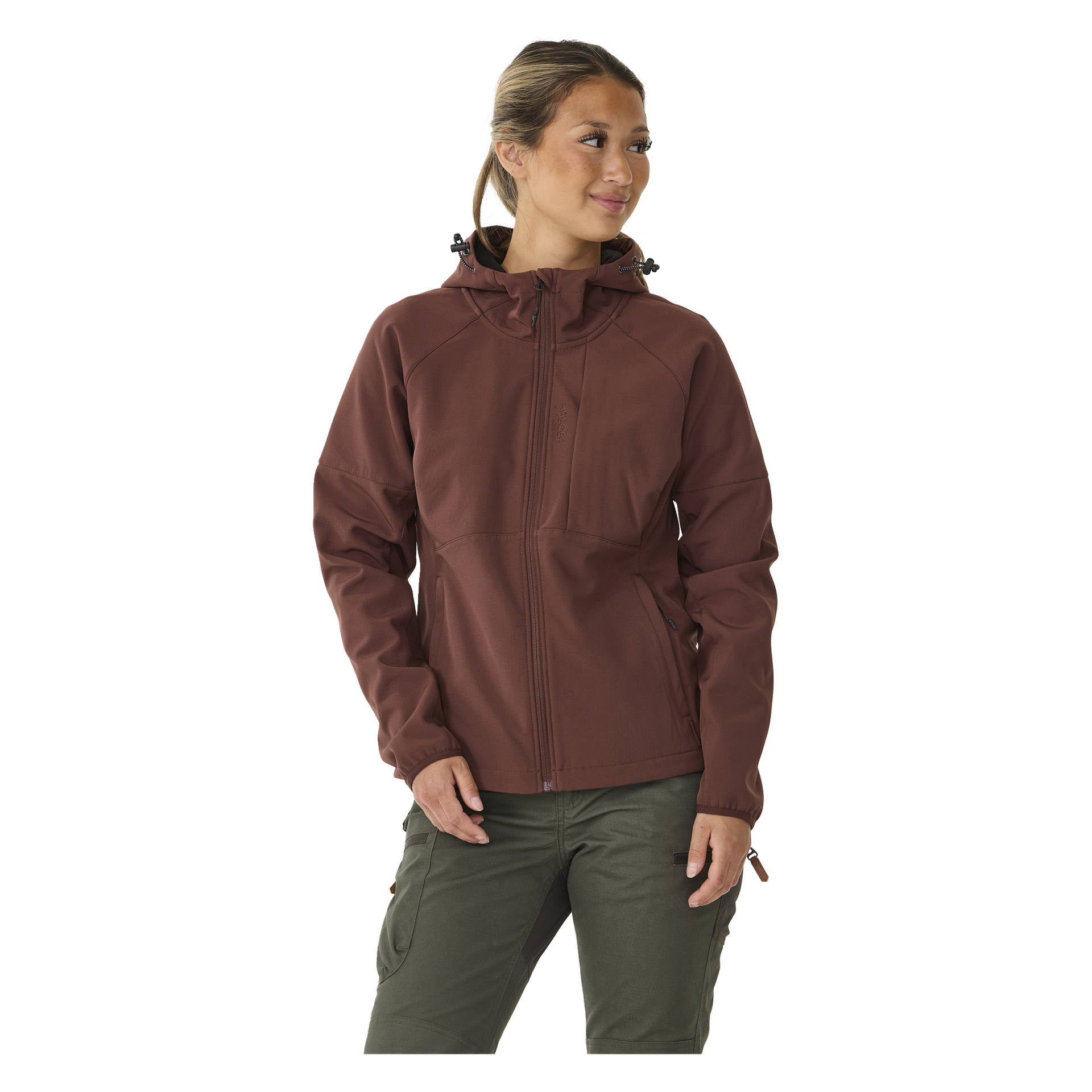 Eine Frau steht leicht nach rechts gedreht, gekleidet in die mit Fleece gefütterte Kayoba Outdoor Softshell-Jacke Hede in Braun und olivgrüne Hosen. Ihr Haar ist zurückgebunden und sie schaut mit neutralem Gesichtsausdruck zur Seite.