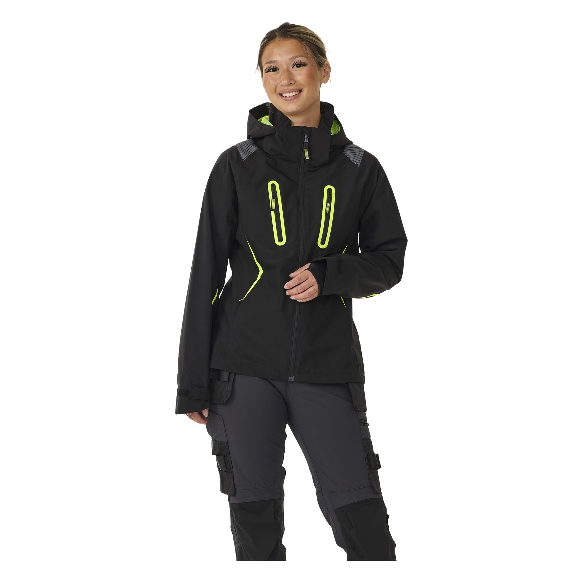 En leende person bär Bluewear Women's stretchjacka Rebecca, en svart jacka med neongula dragkedjor och detaljer, en huva och flera fickor med dragkedja, matchande med mörka verktygsbyxor.