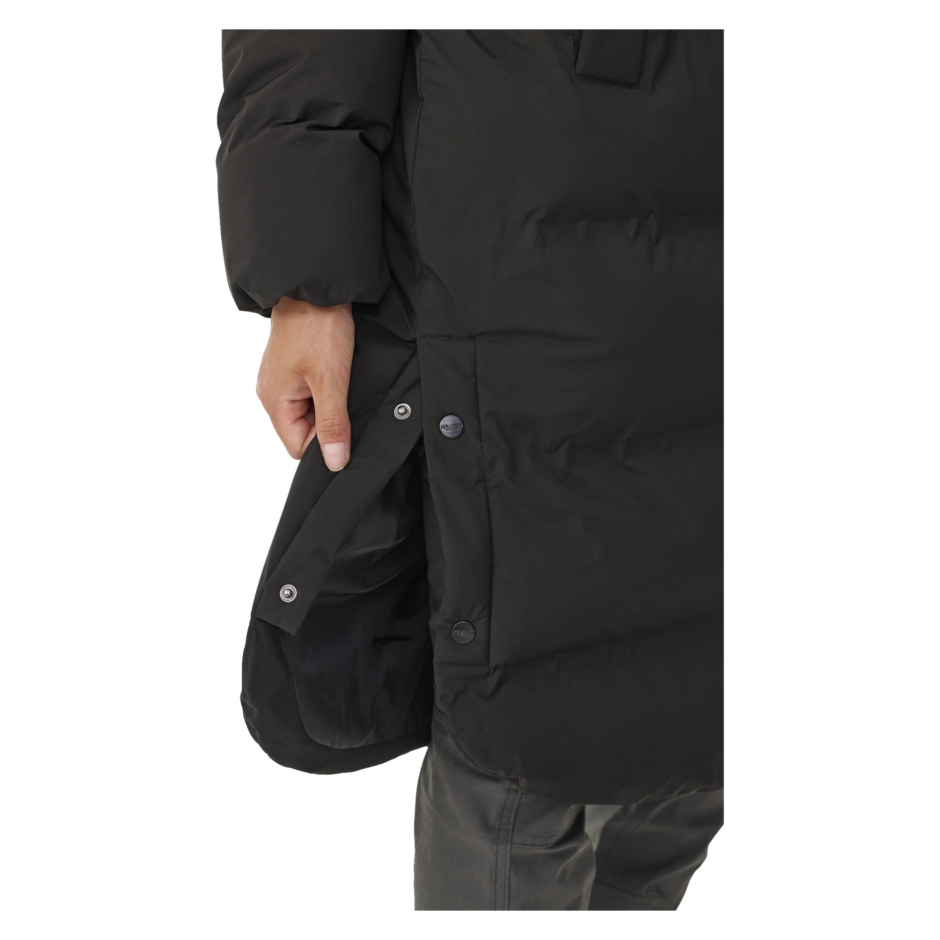 Käsi avaa nappia Kayoba Outdoor Women's Winter Coat Storlienin sivuventtiilissä, ja vain osa takista ja henkilön jalat näkyvät, keskittyen napin yksityiskohtaan.