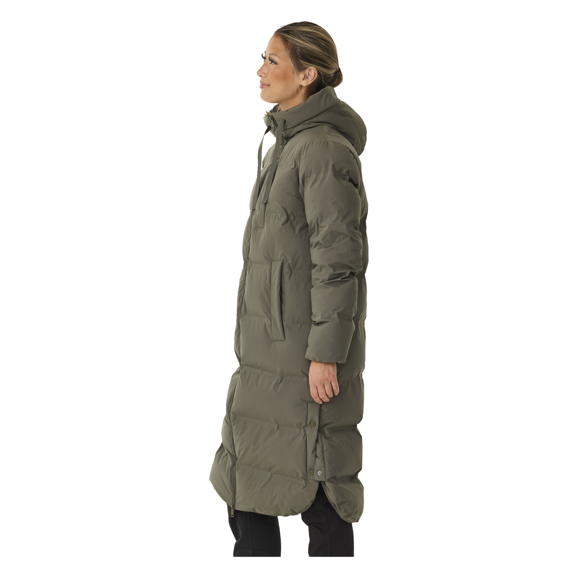 Profiilissa oleva nainen mallintaa Kayoba Outdoor Women's Storlien -talvitakin, pitkän oliivinvihreän pufferin hupulla, tilavilla taskuilla ja tikatulla kuviolla. Hänen hiuksensa on vedetty taakse ja hän katsoo vasemmalle.