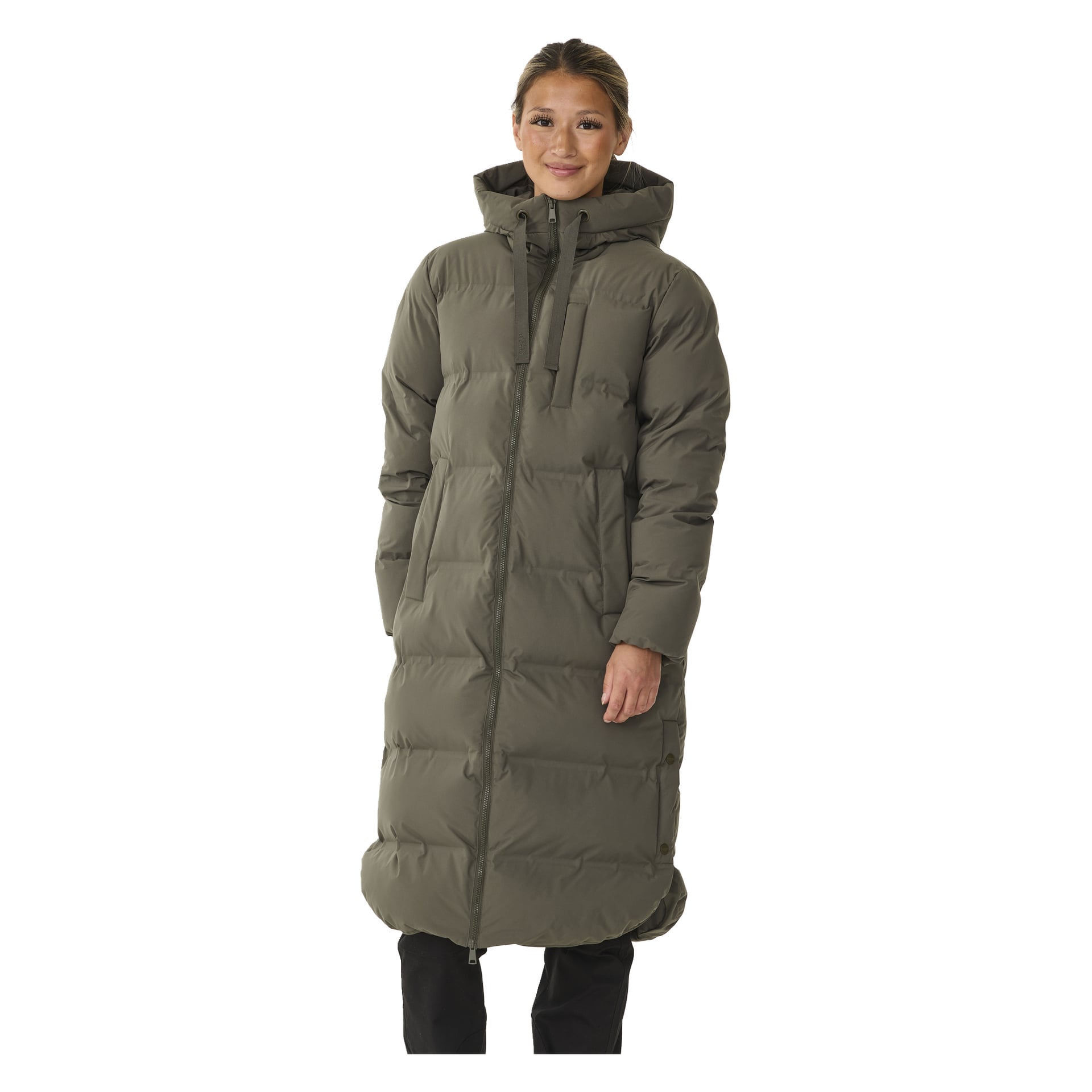 Nainen seisoo hymyillen, pukeutuneena Kayoba Outdoor -naisten talvitakkiin Storlien. Takki on pitkä, oliivinvihreä puffer, jossa on huppu ja etuvetoketju, taskut ja tikattu kuvio, joka ulottuu polvien alapuolelle.