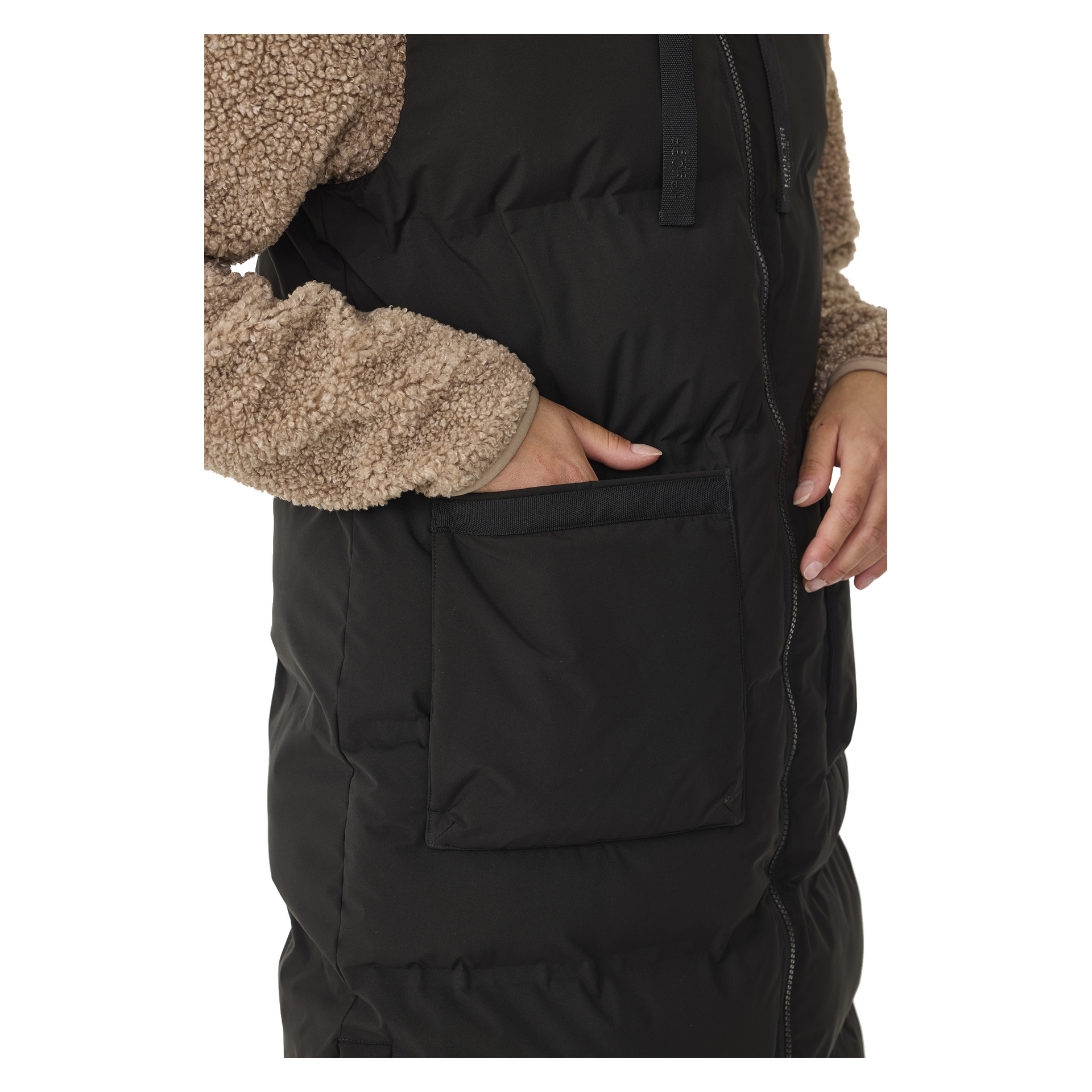 Henkilö, jolla on vaaleanruskea sherpa-hihainen paita, ja Kayoba Outdoor Padded -naisten pitkä Duved-lilet—musta, hihaton liivi, jossa on näkyvä etutasku—on oikea käsi taskussa. Kuva keskittyy vartaloon ja käteen.