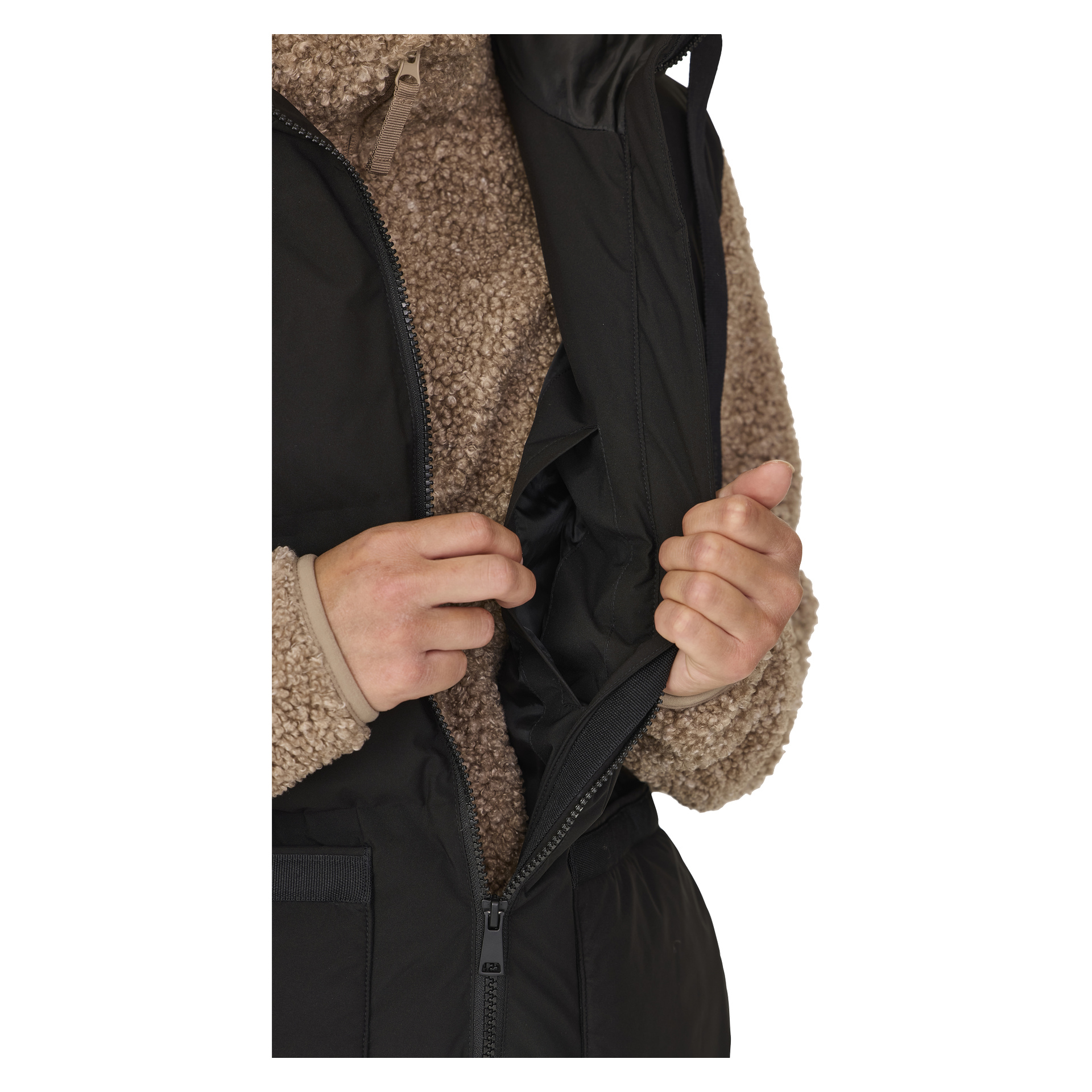 Joku, joka on pukeutunut beige-fleece-takkiin ja mustaan Kayoba Outdoor Pehmustettuun naisten gilet-liikkaan, Long Duved, avaa ja vetää liletin esiin molemmilla käsillään sisätaskun näyttämiseksi; Heidän vartalonsa ja kätensä näkyvät.