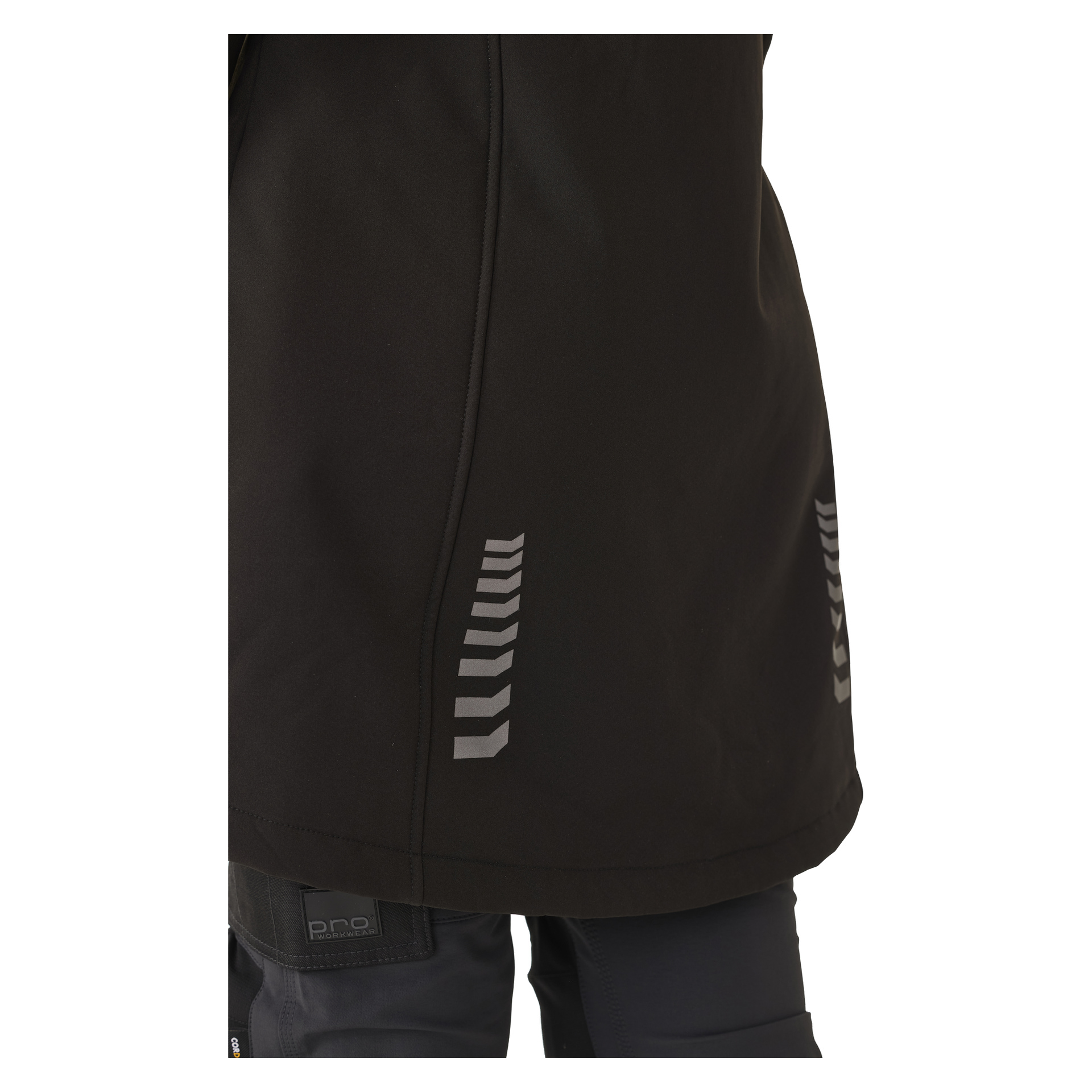 Lähikuvassa näkyy henkilö, joka on pukeutunut Bluewear Womanin pitkään Gunnel-softshell-takkiin mustassa, ja sivulla on useita pieniä heijastavia chevron-yksityiskohtia. Kuvassa näkyy takin alaosa sekä osa heidän ylähousuistaan.