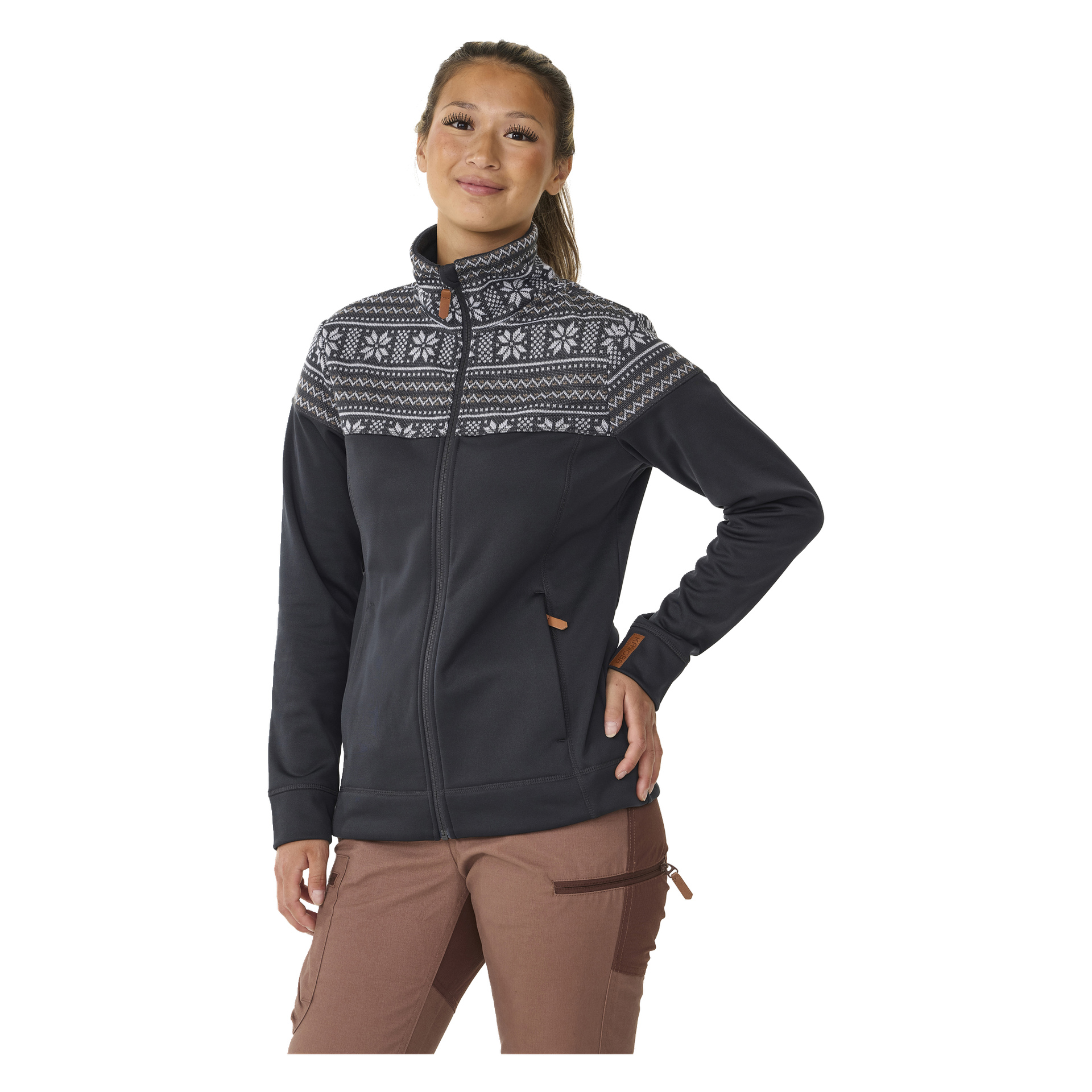 Henkilöllä on päällään Kayoba Outdoor Women's mid-layer -neule Valbo, tumma vaate, jossa pohjoismainen valkoinen kuvio yläosassa ja vetoketjulliset taskut, yhdistettynä ruskeisiin housuihin, joissa on vetoketjullinen tasku.