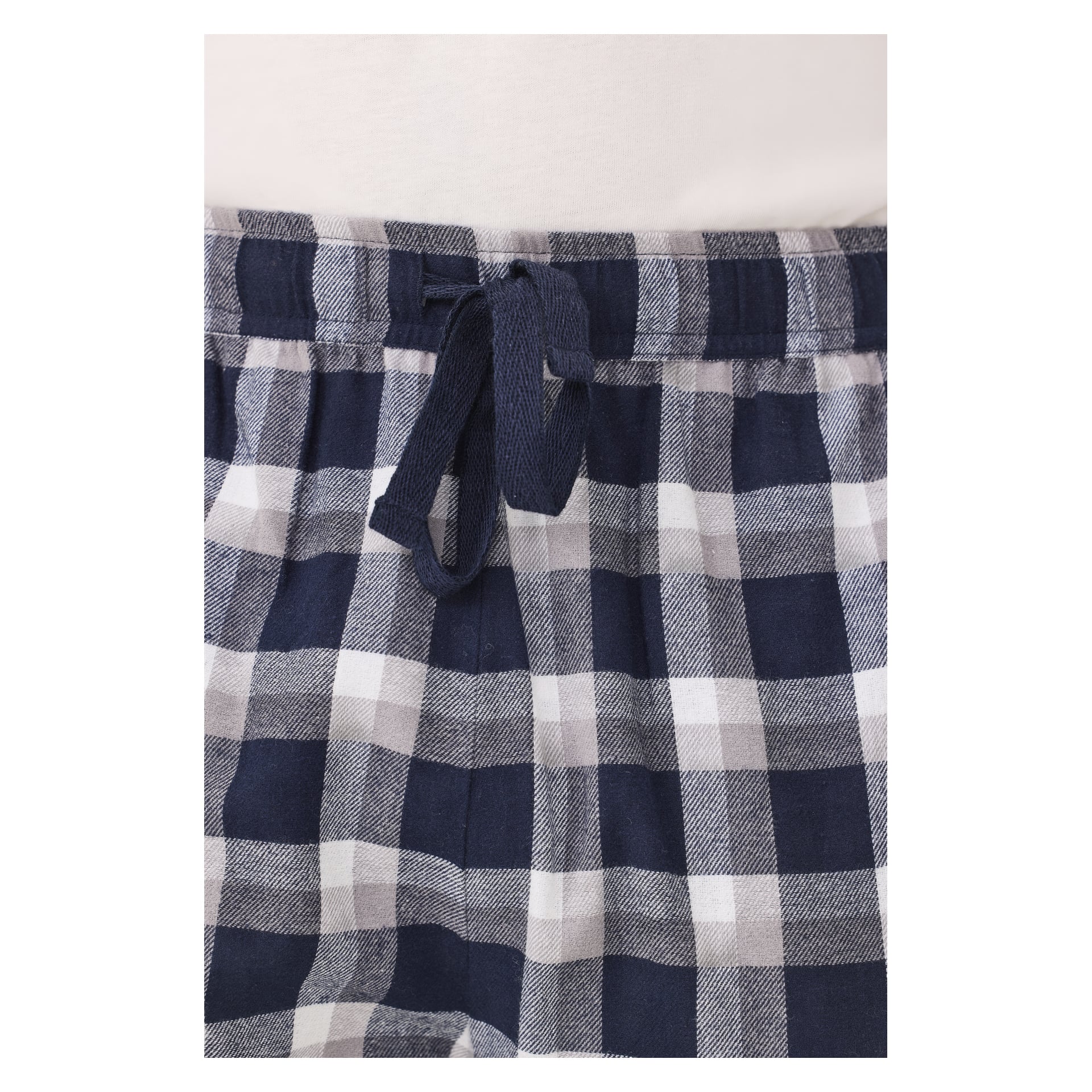Detaljerad vy av en stråke med dragsnöre på midjebandet på Bluewear pyjamasbyxor med blå, grått och vitt rutigt mönster. Den nedre kanten av en lätt skjorta syns ovanför midjebandet.