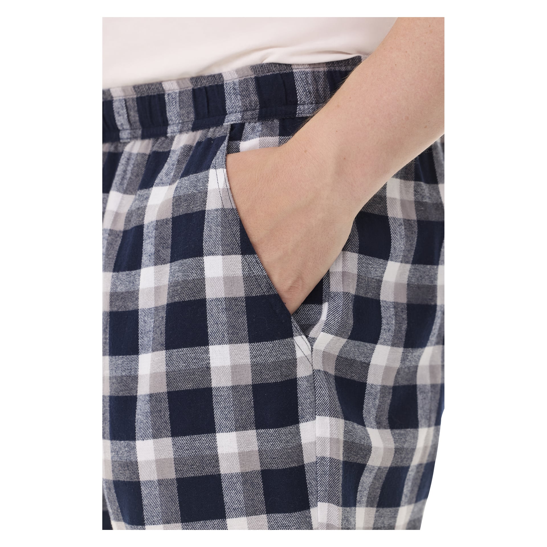 En hand är instucken i fickan på Bluewear-pyjamasbyxor med ett blå, vitt och grårutigt mönster. Byxorna har ett elastiskt midjeband, och en del av en vit skjorta syns ovanför dem.