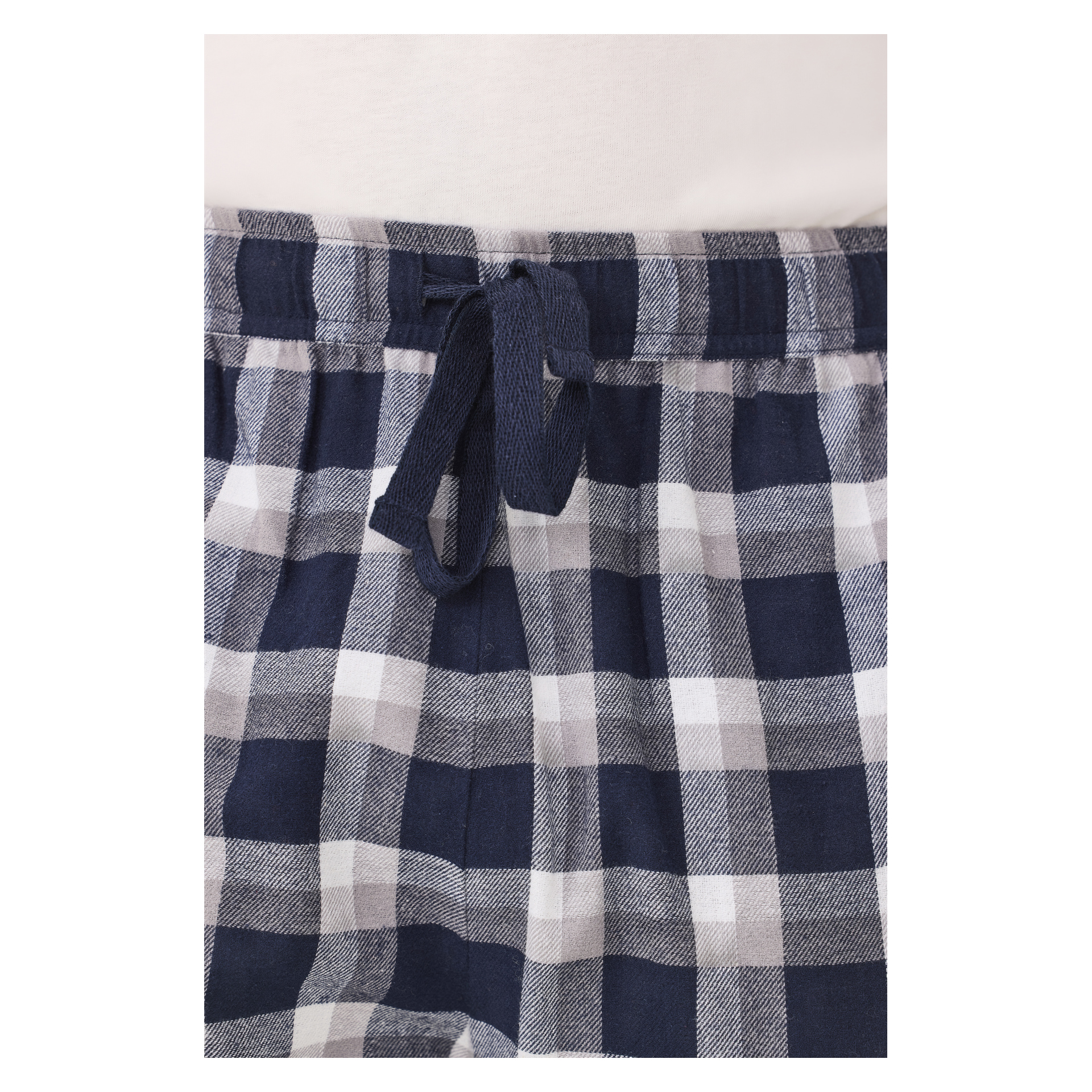 En närbild av Bluewear Pyjamasbyxor visar det blå, grå och vita rutiga midjebandet med en dragsko knuten i en enkel knut. Den nedre kanten av en vit skjorta syns upptill.