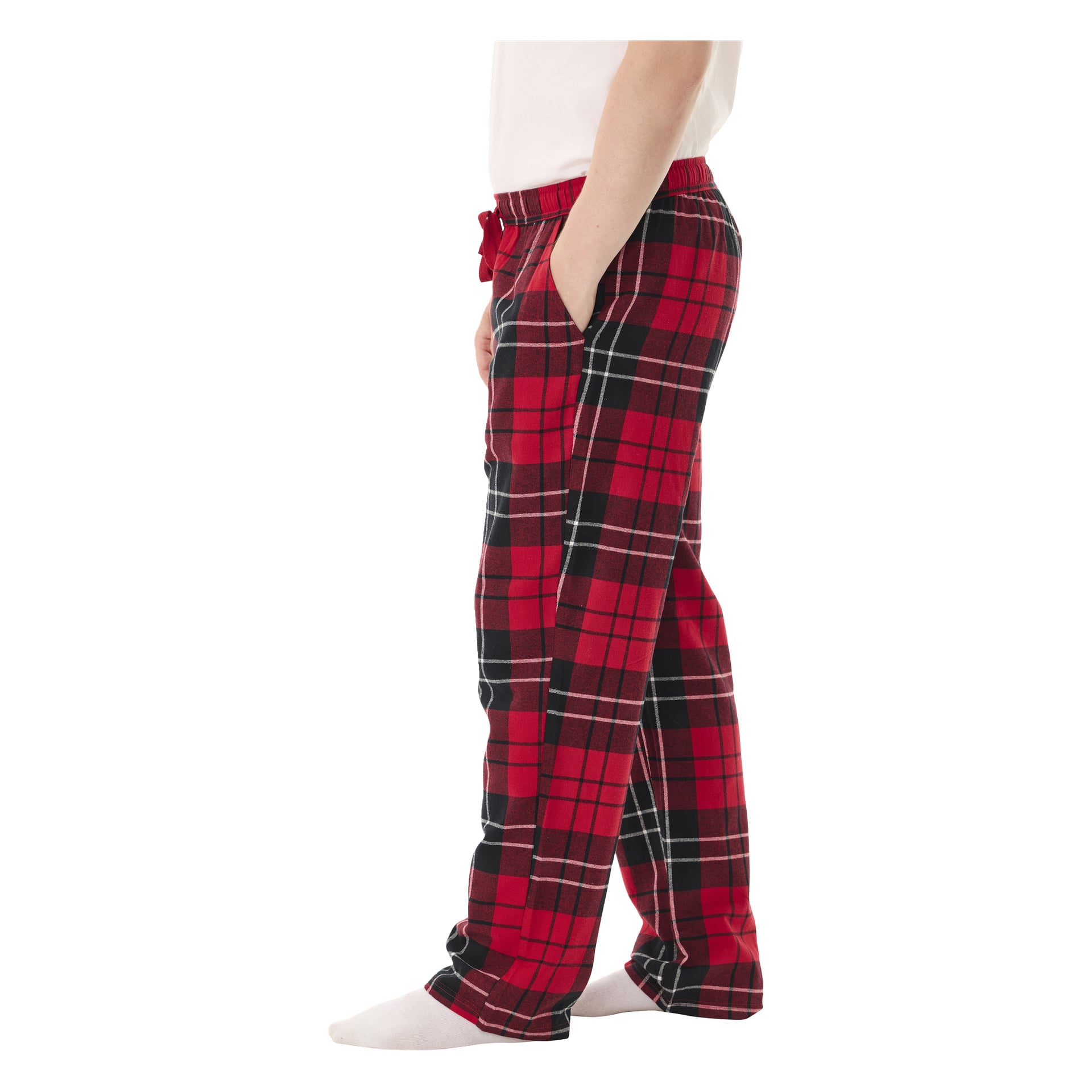 En person står barfota i Bluewear-pyjamasbyxor med rödrutigt mönster, tillsammans med en vit skjorta. De ses från sidan med ena handen i fickan.