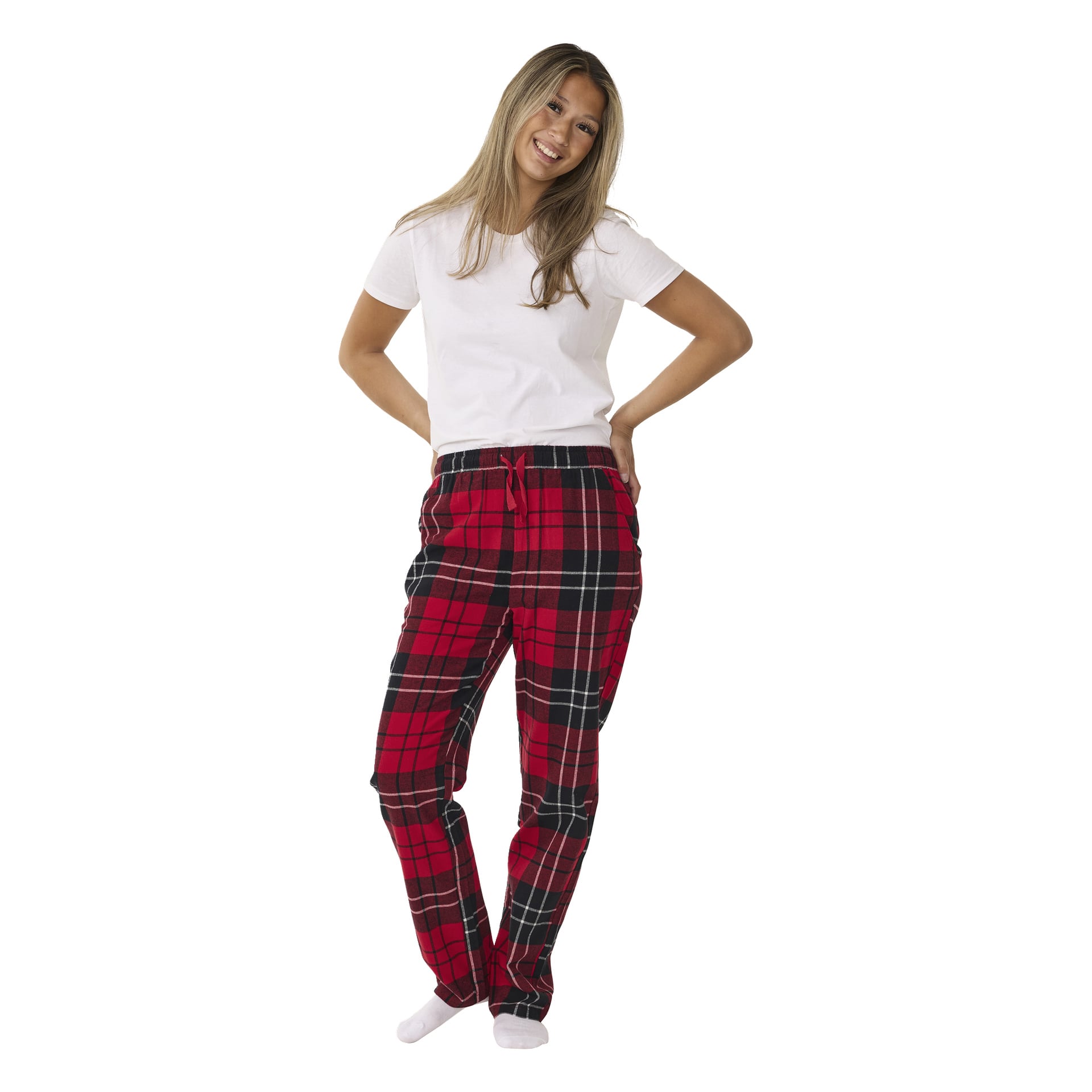 En leende person står med händerna i fickorna på Bluewear-pyjamasbyxor med röd rutig design och midja med dragsko, tillsammans med en enkel vit t-shirt och vita strumpor.