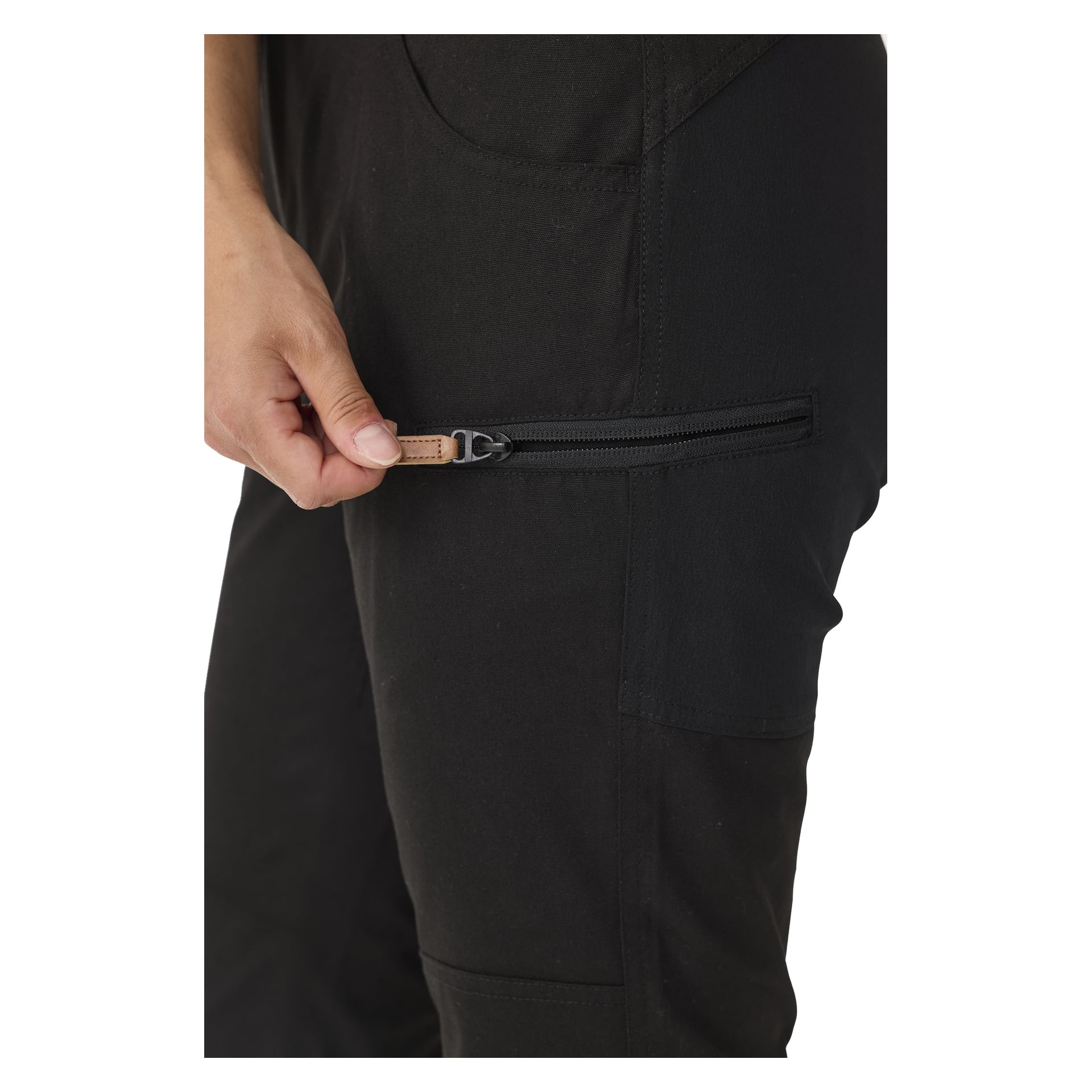 Henkilö käyttää oikeaa kättään avatakseen vaakasuoran vetoketjun, jossa on pieni ruskea vetolipu mustien Kayoba Outdoor Leisure Women's Älvdalen 2.0 -housujen sivutaskussa.