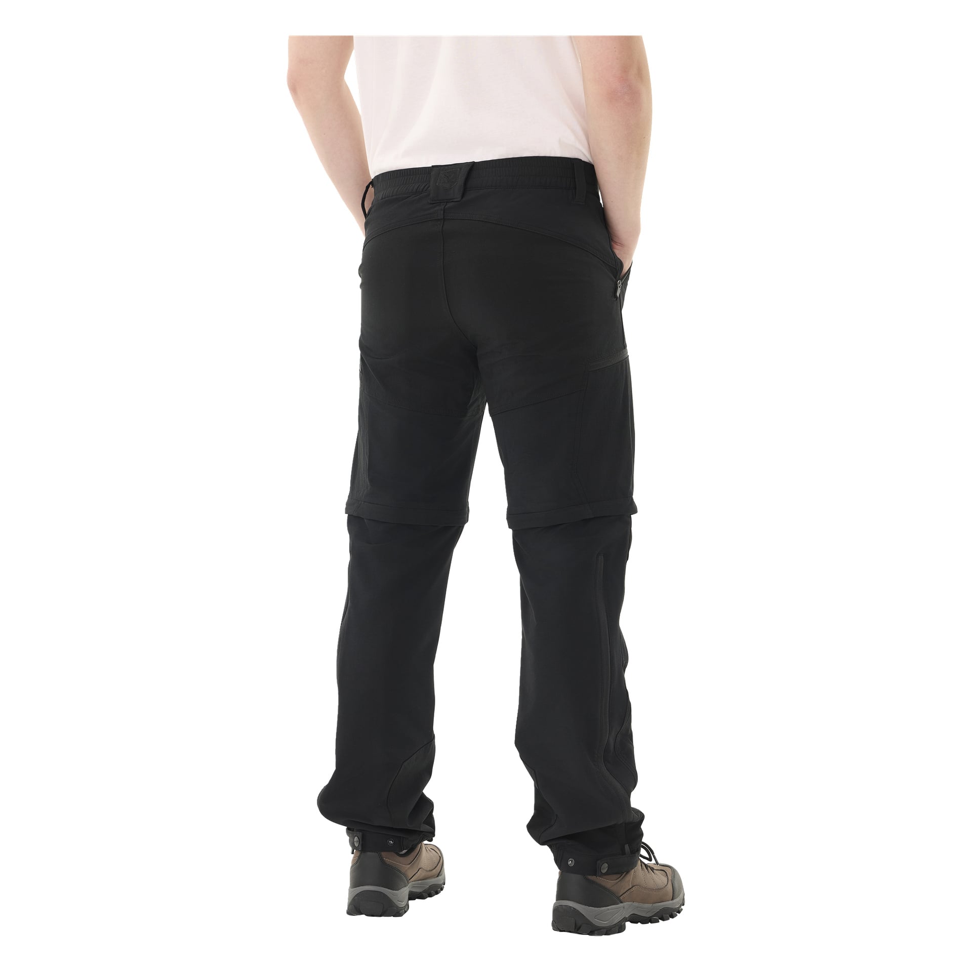 En person står med händerna i fickorna, vänd bort från kameran, klädd i svarta Kayoba Outdoor Men's dragkedda utebackbyxor, en lätt skjorta och bruna vandringskängor.