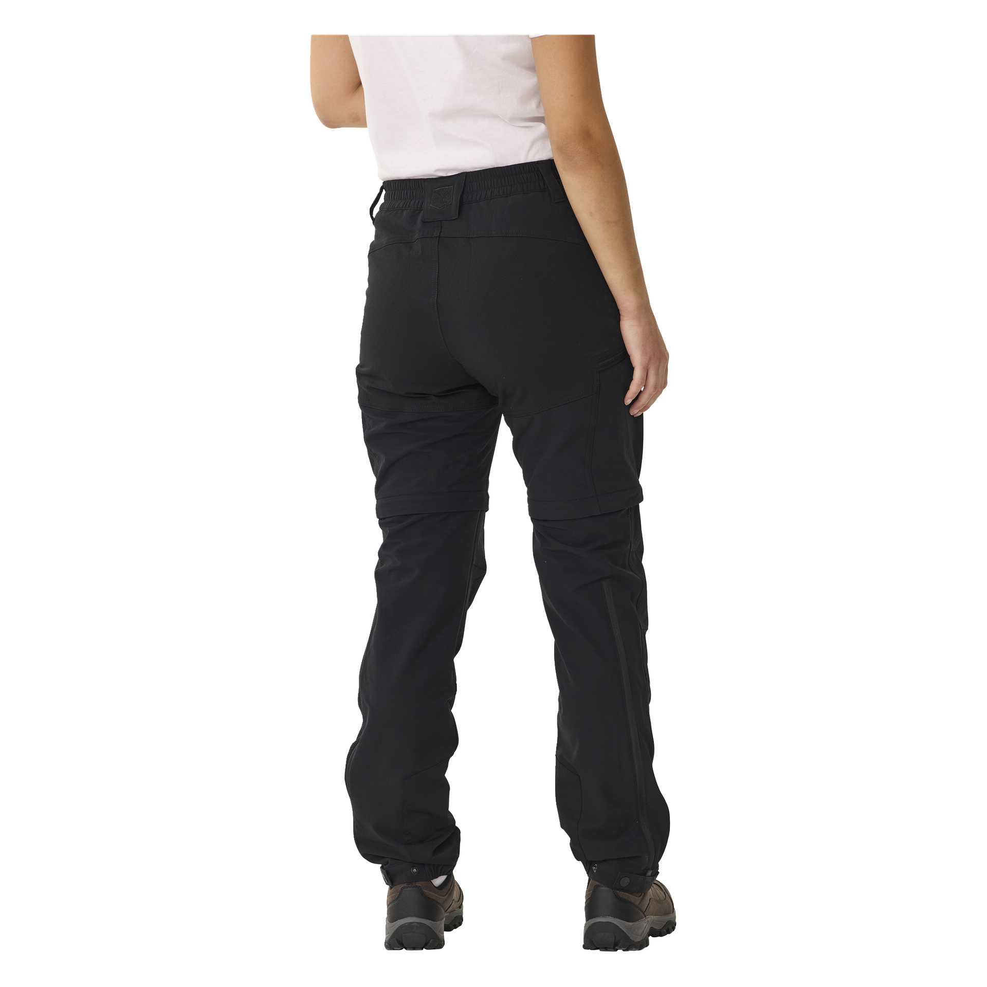 Od tyłu widziana jest osoba w białej koszulce z krótkim rękawem, czarnych męskich spodniach Kayoba Outdoor Abisko na zip oraz butach trekkingowych, widoczna od ramion po stopy.