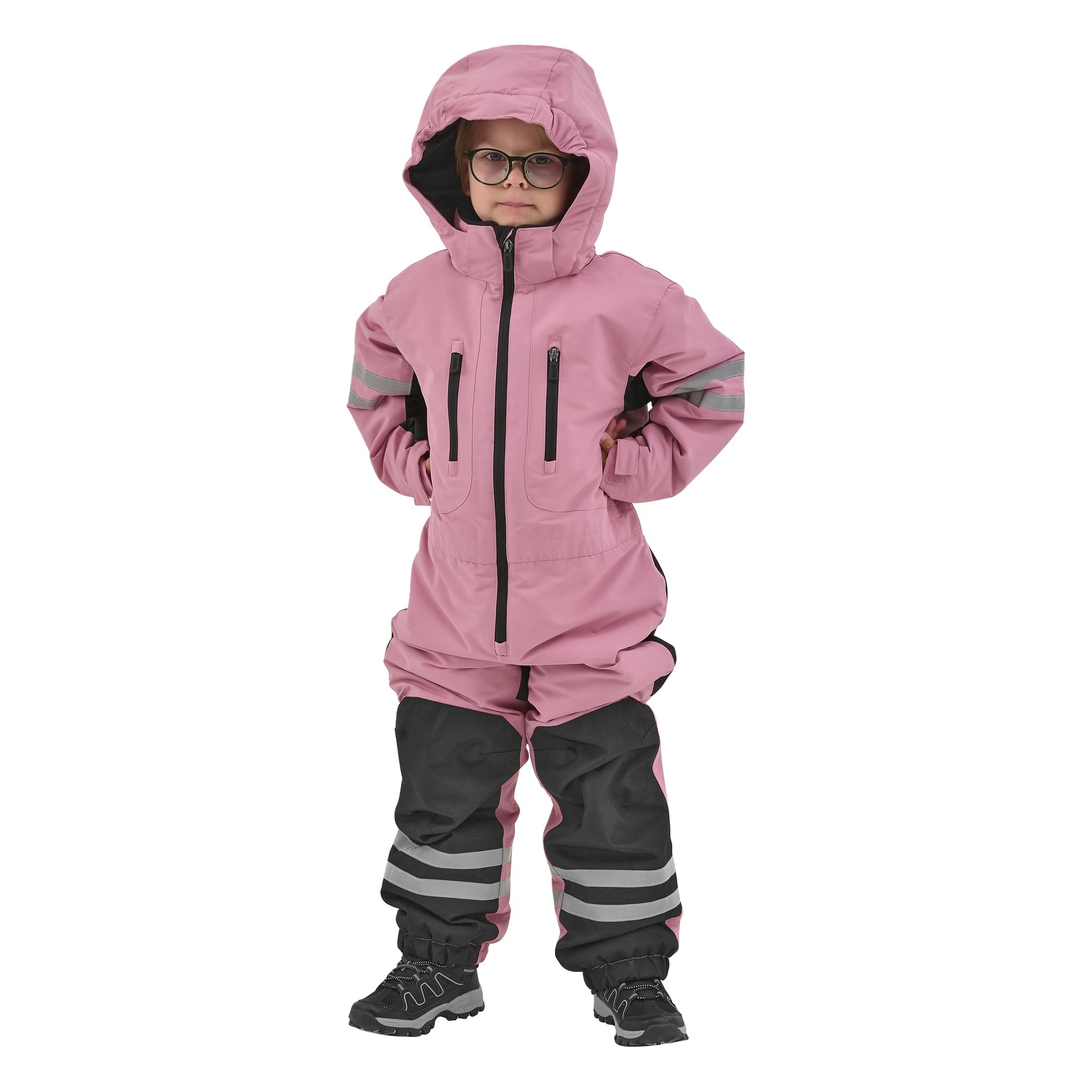Ett litet barn med glasögon står självsäkert, händerna på höfterna, klädd i en Kayoba Outdoor Dundret rosa snöoverall med svarta detaljer på benen och bär svarta skor. Dräkten har reflekterande ränder på ärmar och ben.