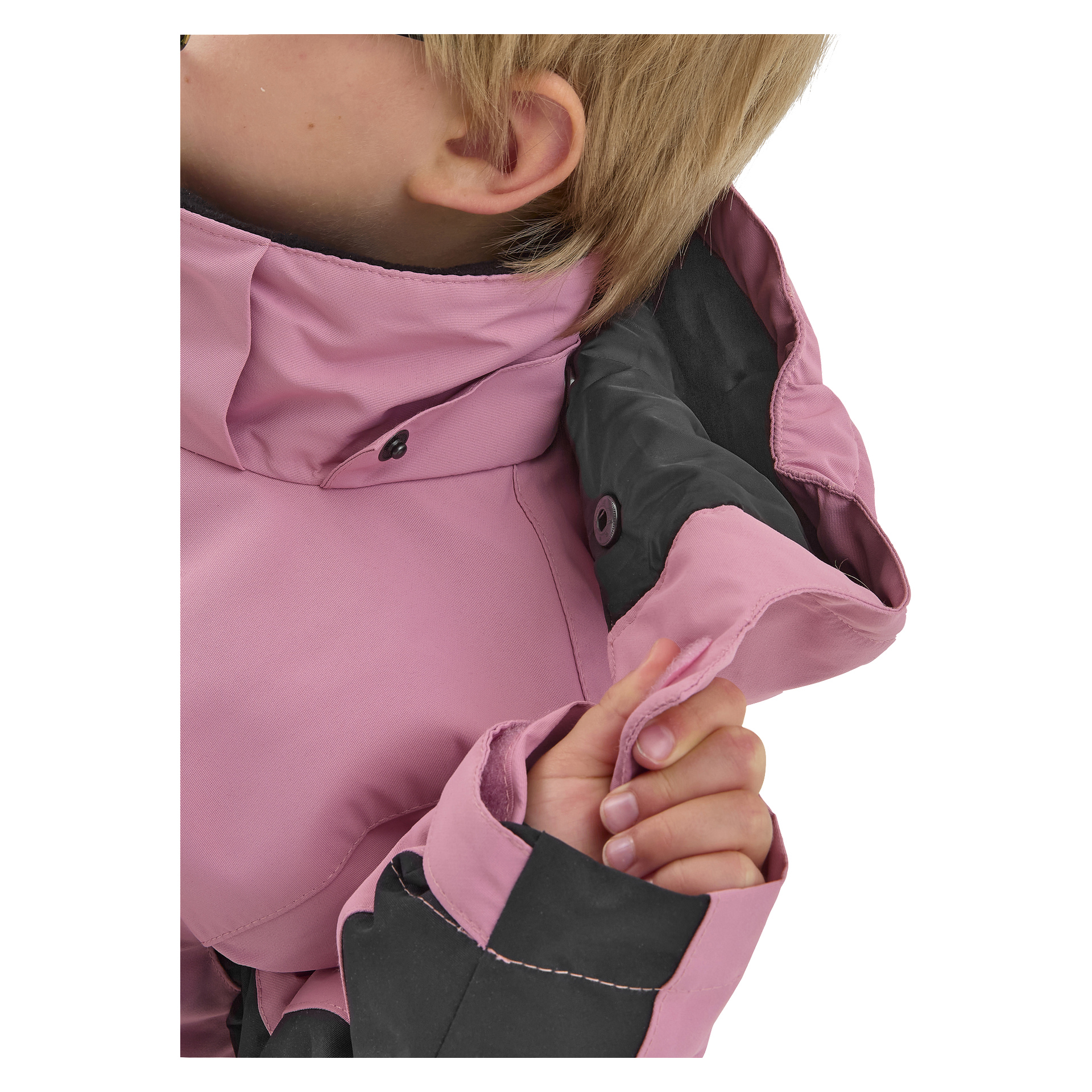 Ett ljust hårigt barn visar den rosa och svarta Dundret-jackan från Kayoba Outdoor, lyfter kragen för att visa dess interiör. Barnets ansikte är mestadels utanför bildrutan.