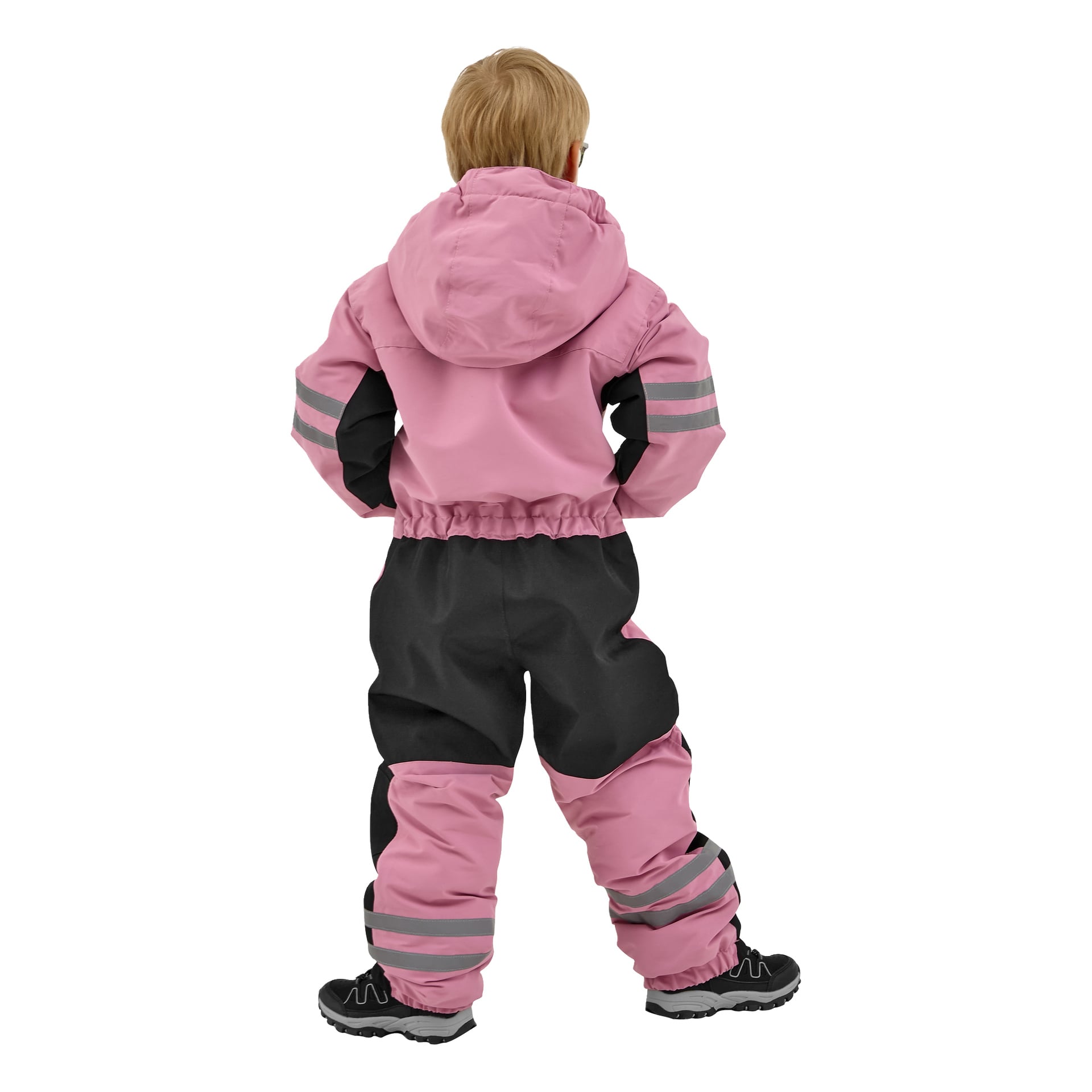 Ett litet barn med ljust hår syns bakifrån, klädd i en Kayoba Outdoor Dundret snödräkt som är rosa och svart med reflekterande ränder på ärmar och byxben, och bär svarta skor med tjocka sulor.