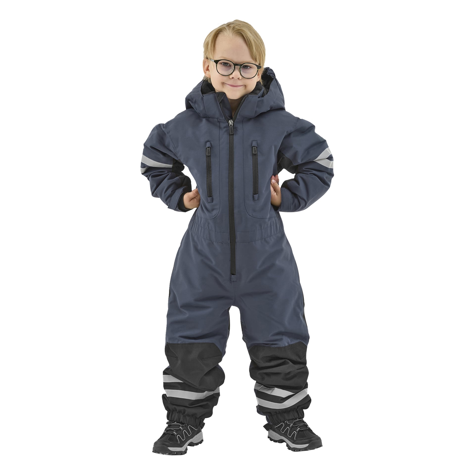 Ett barn med glasögon står leende, klädd i en Kayoba Outdoor Dundret mörkblå huva med reflekterande ränder på ärmar och ben, ihopspelad med svarta skor.