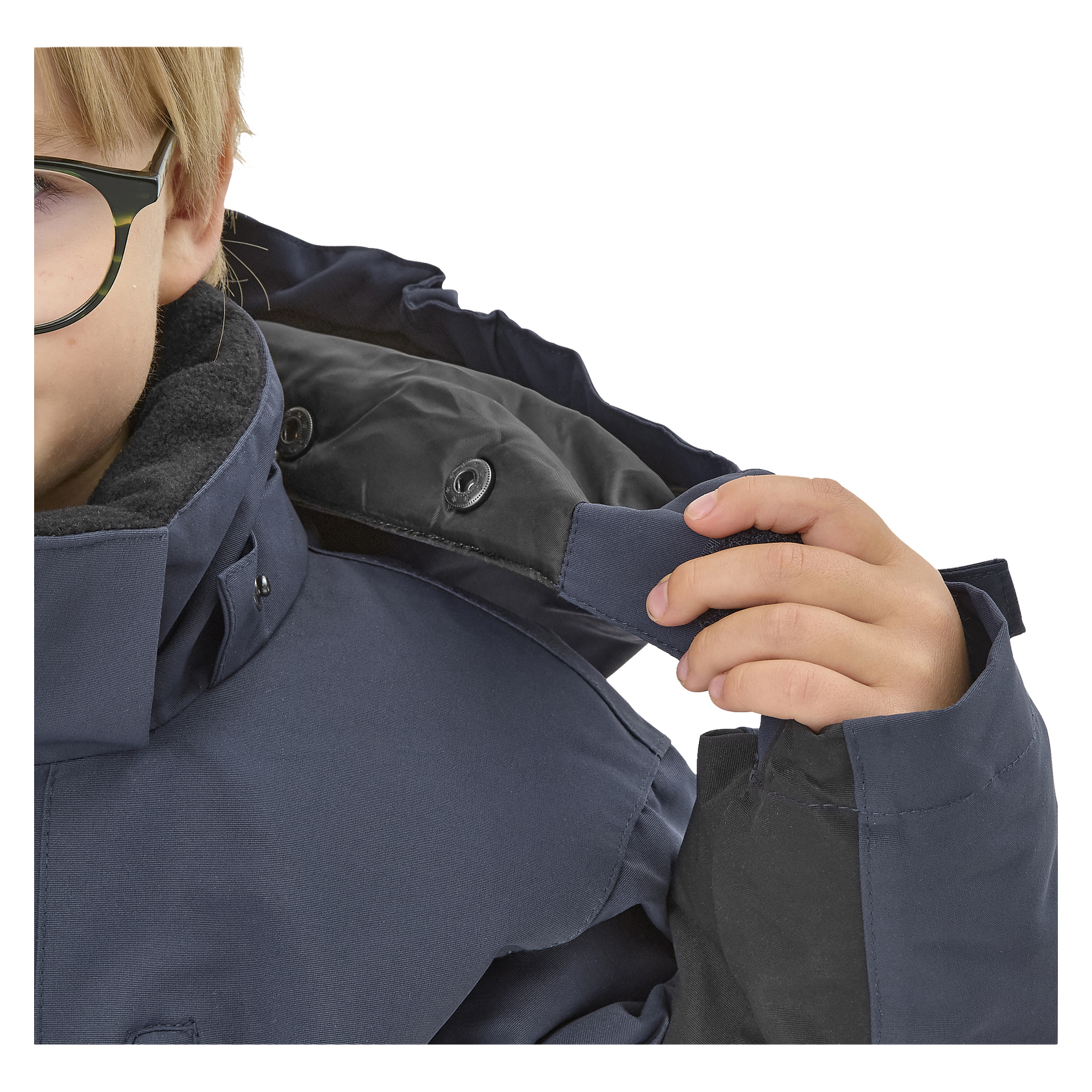 Ett barn med glasögon och en Kayoba Outdoor Dundret marinblå vinterjacka lyfter huvan med ena handen och visar jackans material och dess svarta fleeceinsida. Endast en del av barnets ansikte kan ses.