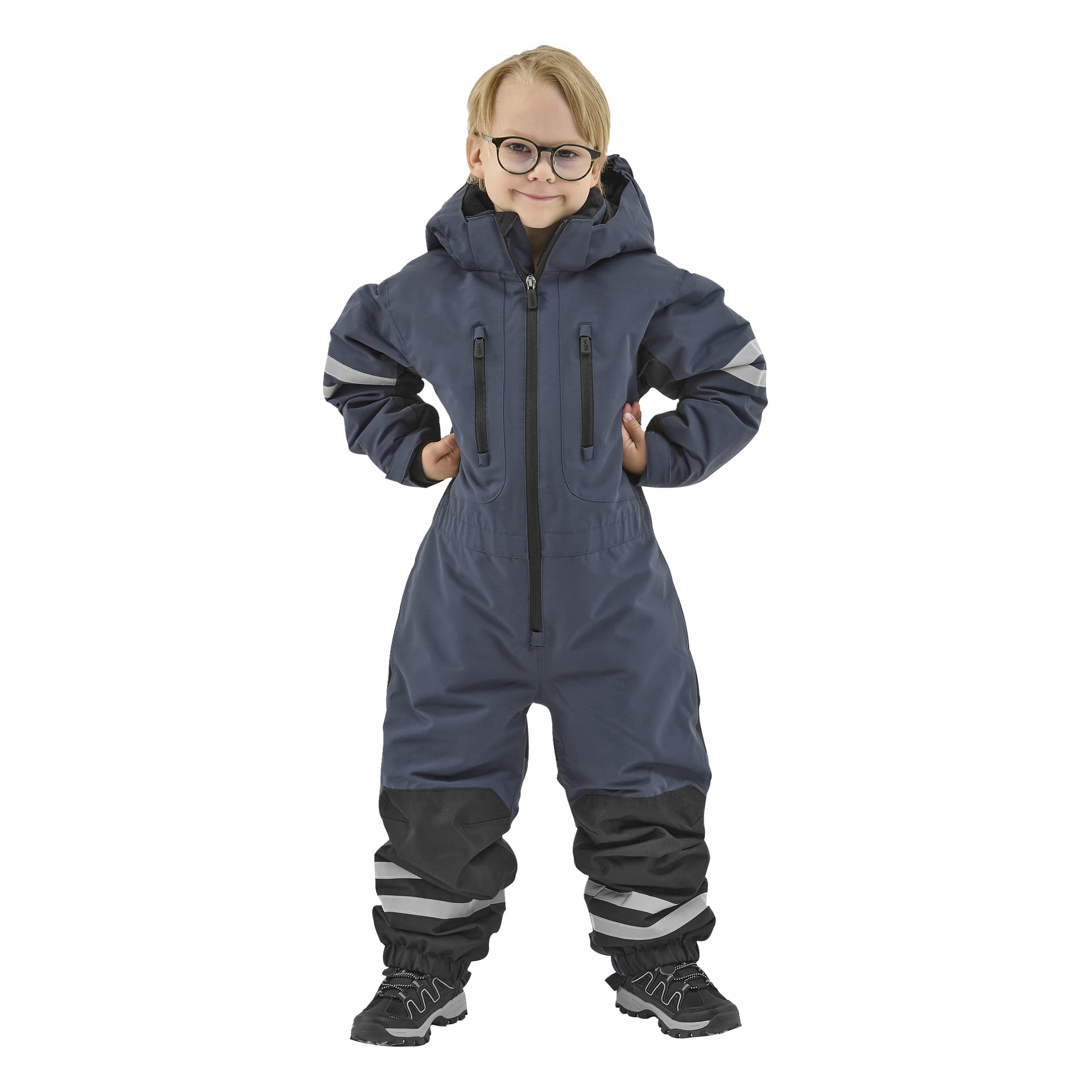 Ein Kind mit Brille steht nach vorne in einem blauen Kayoba Outdoor Dundret Schneeanzug mit schwarzen Akzenten und reflektierenden Elementen. Das Einteiler-Outfit verfügt über Kapuze, Reißverschlüsse und wird mit schwarzen Schuhen kombiniert.