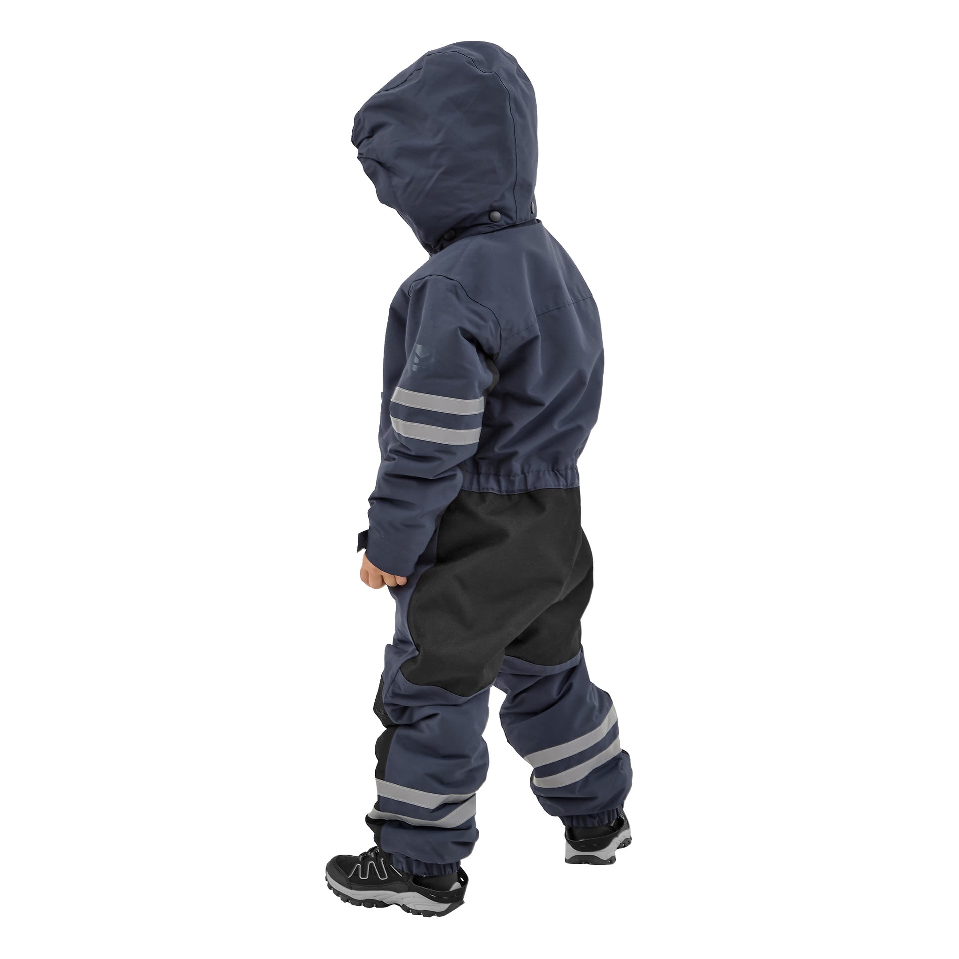 Ein Kind ist von hinten zu sehen, gekleidet in eine dunkelblaue Kayoba Outdoor Dundret Kapuzenjacke und passende Hosen mit reflektierenden Streifen. Der Anzug verfügt über schwarze Patches an den Knien und am Sitz, kombiniert mit schwarzen Turnschuhen mit weißen Sohlen.