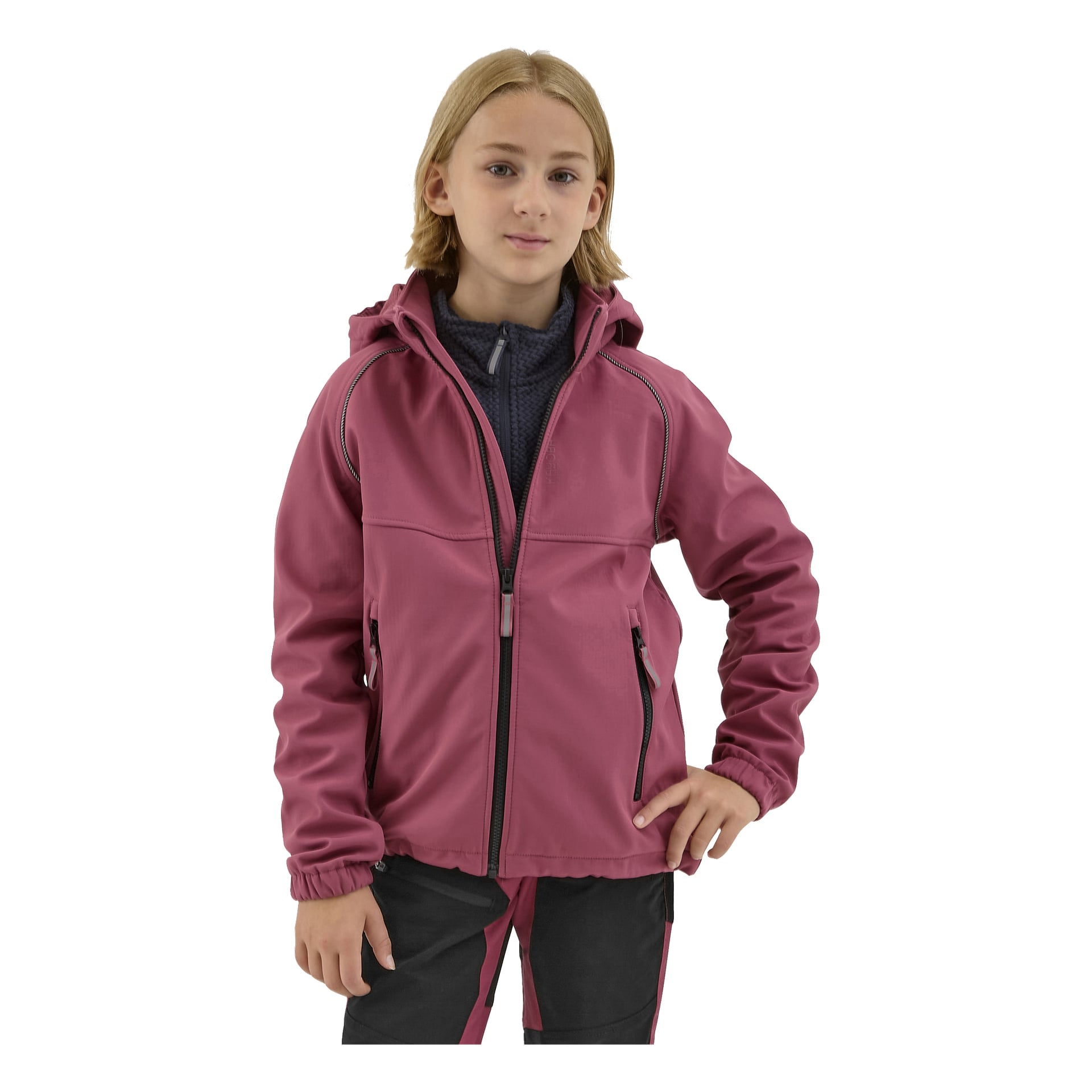 Nuori, jolla on olkapäille ulottuvat vaaleat hiukset, on pukeutunut vaaleanpunaiseen Kayoba Outdoor Children's softshell -takkiin Kramforsiin, tummat housut ja seisoo itsevarmasti, toinen käsi lanteilla.