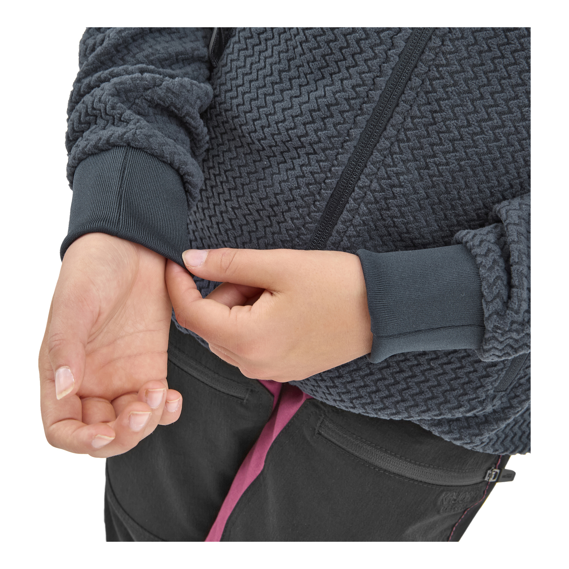 Joku, joka on pukeutunut Kayoba Outdoor Children's fleece -takkiin Omberg, jossa on teksturoitu tummanharmaa kuvio ja mustat housut, säätää hihansettiaan yhdellä kädellä. Niiden kynnet pidetään lyhyinä eikä niissä ole lakkaa.