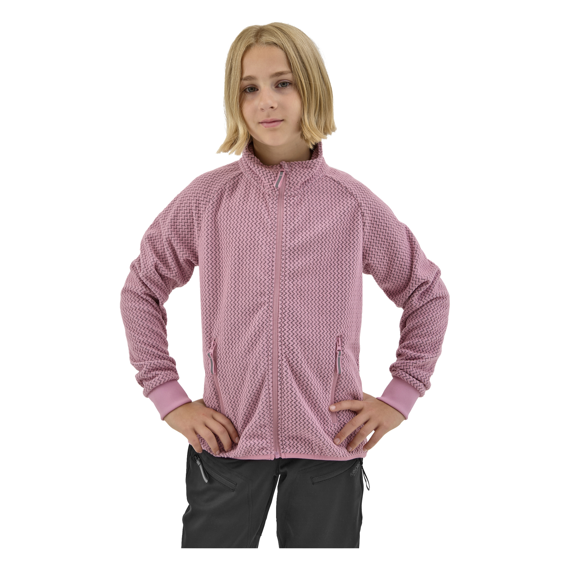 Nuori henkilö, jolla on olkapäille ulottuvat vaaleat hiukset, seisoo kädet lanteilla, yllään Kayoba Outdoor Children's fleece -takki Omberg — vaaleanpunainen teksturoitu vetoketju — ja mustat housut.