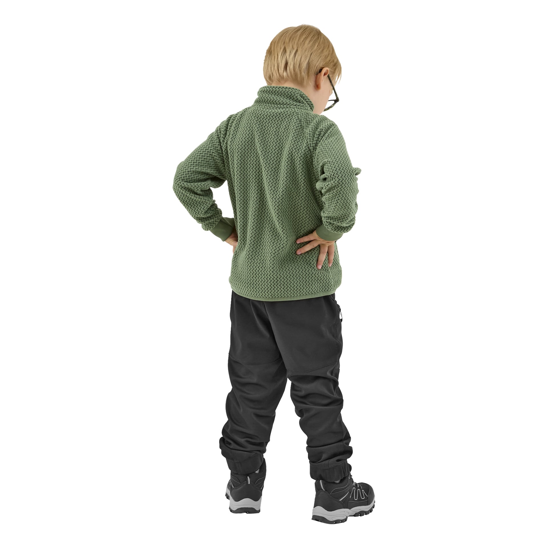 Lyhyt vaaleahiuksinen lapsi kääntyi pois, pukeutuneena silmälaseihin ja vihreästi kuvioituun Kayoba Outdoor Children's Omberg -fleecetakkiin, mustiin housuihin ja mustiin lenkkareihin. Kädet lanteilla lapsi katsoo hieman oikealle.
