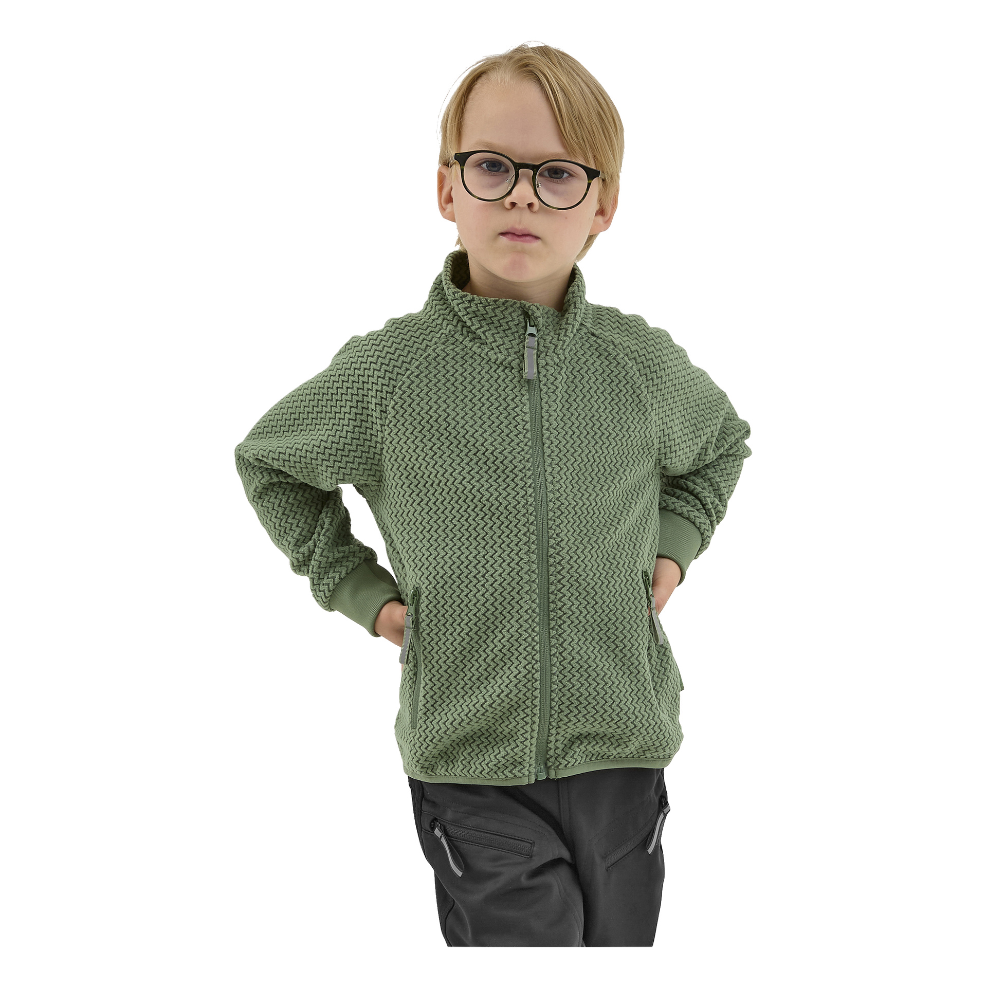 Nuori lapsi, jolla on lyhyet vaaleat hiukset ja silmälasit, seisoo kädet lanteilla, pukeutuneena vihreään Kayoba Outdoor Children's fleece -takkiin Omberg ja tummiin housuihin, katsoen suoraan kameraan.