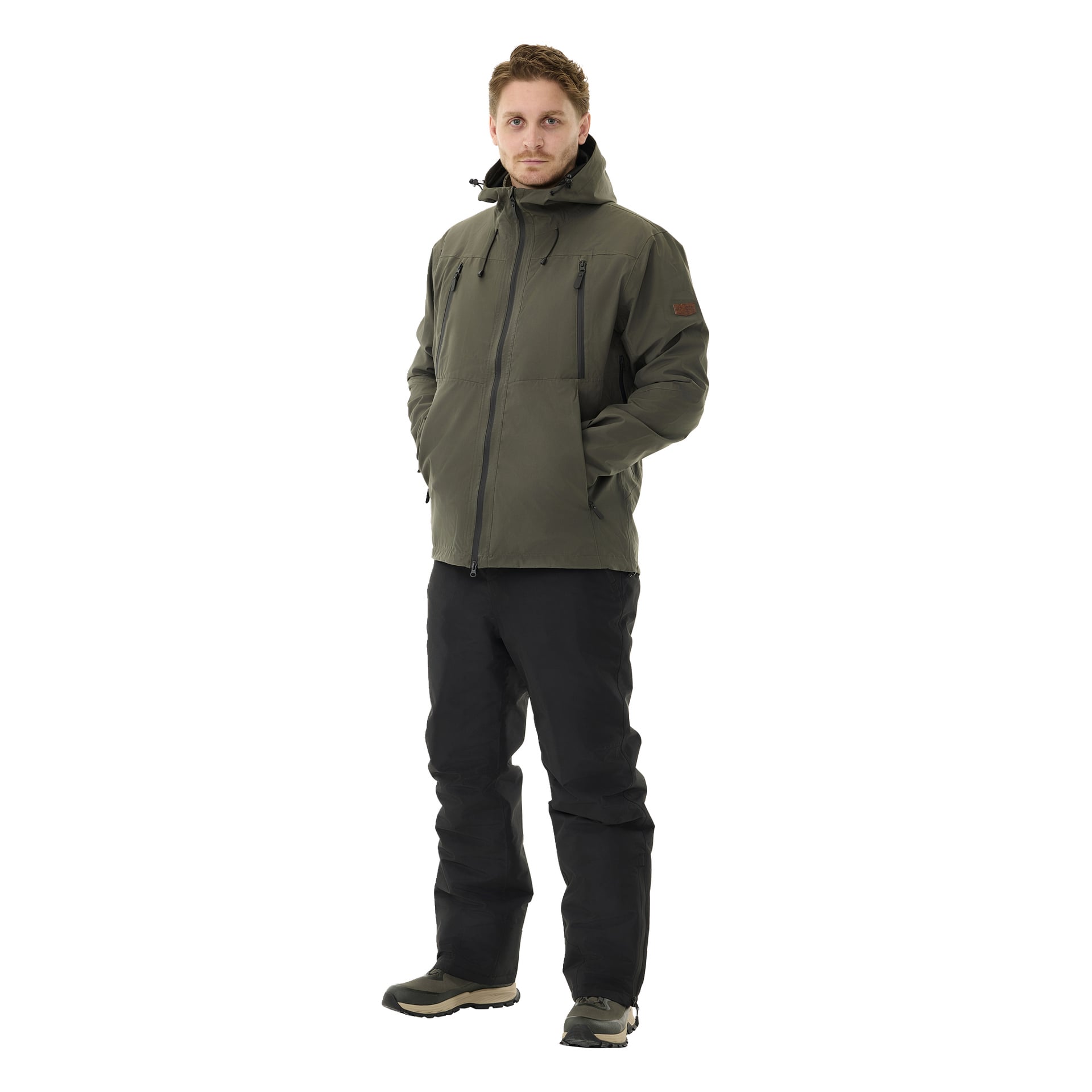 Mies seisoo kasvot eteenpäin neutraali ilme kasvoillaan, kädet vihreän hupparitakin taskuissa. Hän käyttää Kayoba Outdoor -pehmustettuja miehille Kiruna 2.0 -housuja ja ruskeapohjaisia kenkiä.
