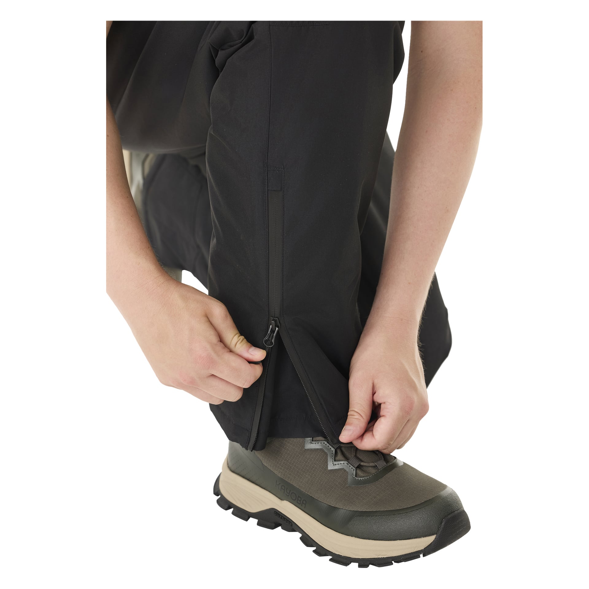 Joku avaa Kayoba Outdoor Padded Kiruna 2.0 -miesten housujen alaraajaosan vetoketjun ja hänellä on harmaat ja beiget vaelluskengät.