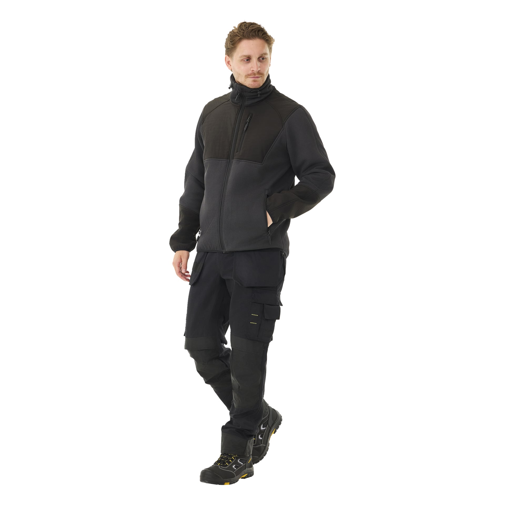 Henkilöllä on yllään Bluewear Men's Morten -kasallinen fleecetakki, yhteensopivat mustat cargo-housut taskuineen ja mustat työkengät, joissa on keltainen koroste. He katsovat hieman sivulle, toinen käsi takin taskussa.