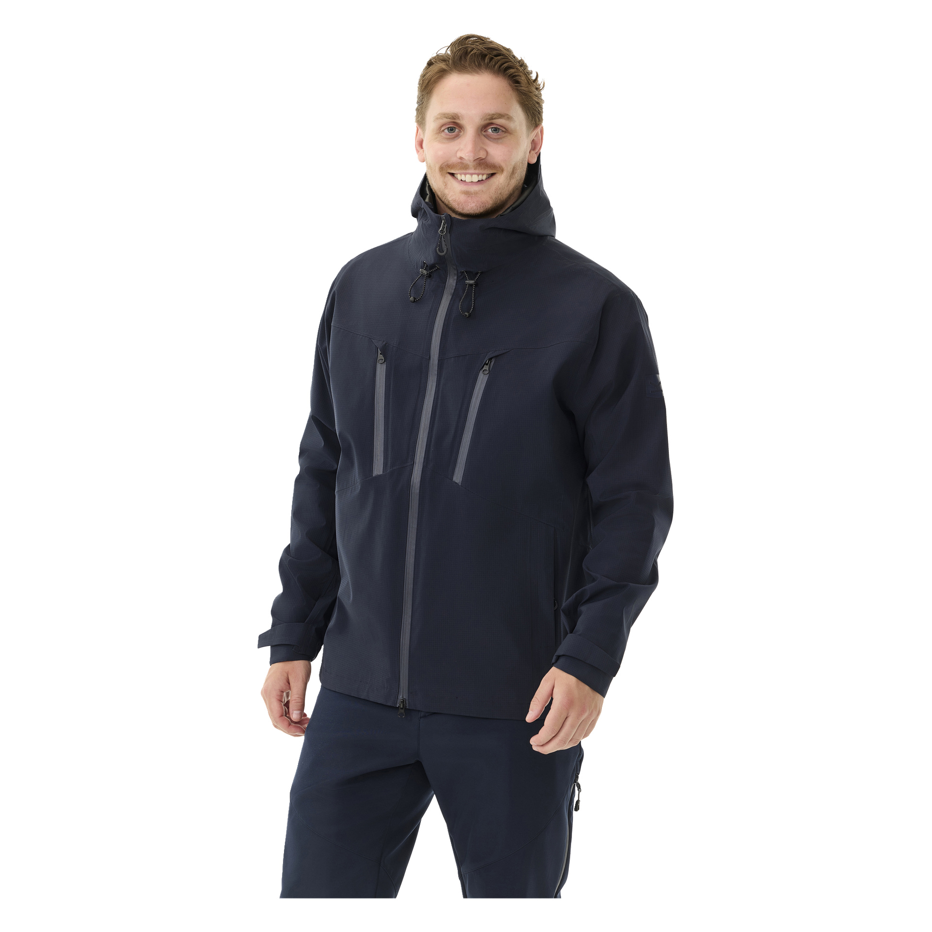 En mann med lyst brunt hår og skjegg er kledd i Kayoba Outdoor Men's Shell Jacket Sarek i marineblått, sammen med matchende bukser. Han står vendt mot kameraet og smiler.