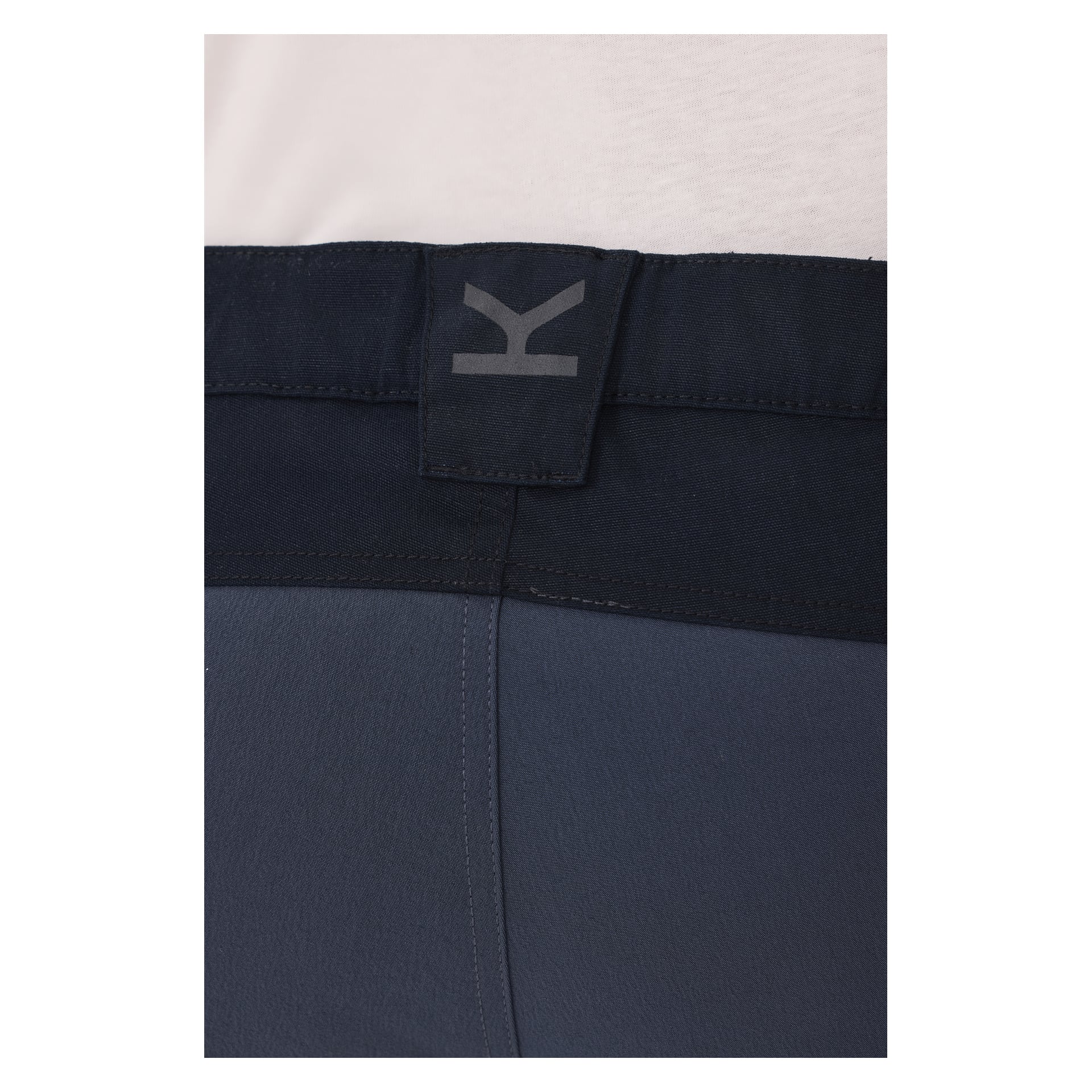 Eine detaillierte Ansicht des Bund der blauen Kayoba Outdoor Men Älvdalen 2.0 Hosen, die eine schwarze Gürtelschlaufe mit einem grauen K-Logo zeigt. Der obere Rand eines weißen Hemdes lugt über dem Bund hervor.