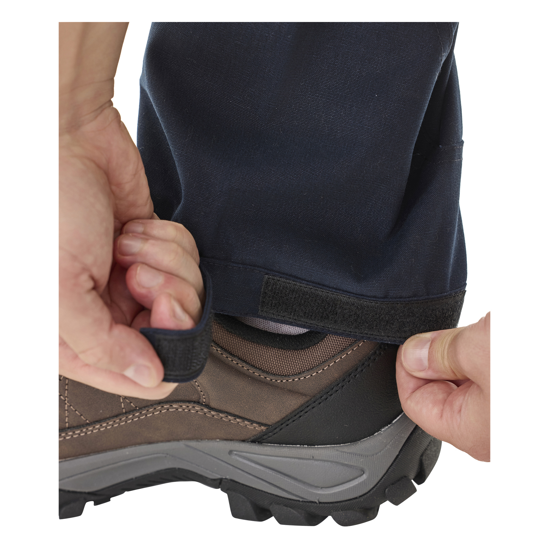 Man fäster kardborrebandet vid fållen på Kayoba Outdoor Men's Outdoor Outdoor Trousers Älvdalen 2.0 runt vristen och fäster det över en robust brun vandringssko. Bilden betonar händerna och underbenet.