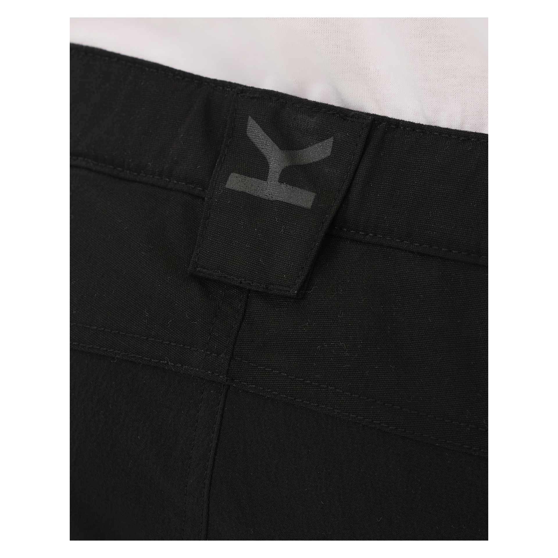 Detaillierte Ansicht des Hosenbunds der Kayoba Outdoor Men Älvdalen 2.0 Hosen in Schwarz, mit einem schwarzen Loop-Tag und einem dunkelgrauen Logo. Ein Teil eines weißen Hemdes ist oberhalb des Hosenbunds zu sehen.
