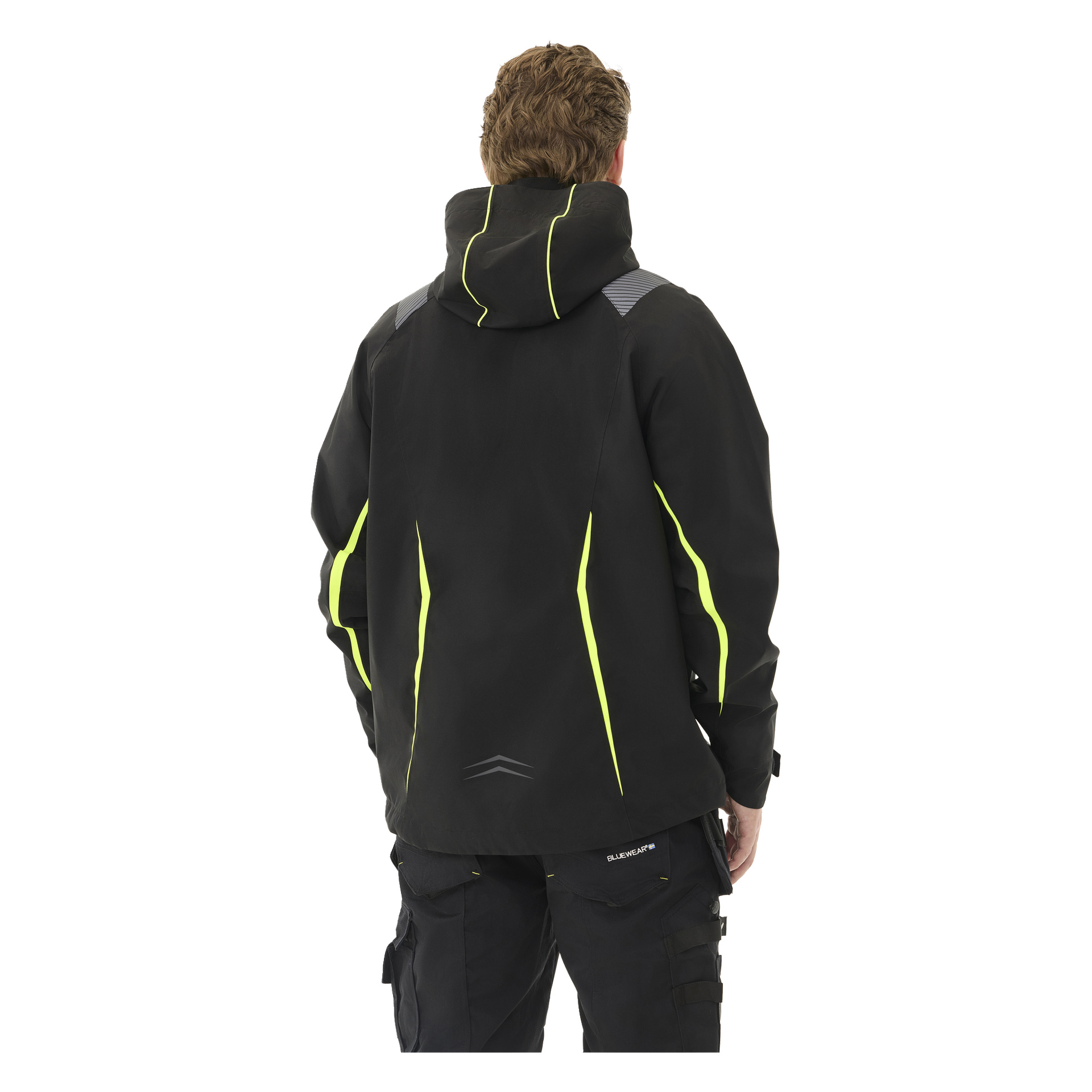 Sedd bakifrån bär personen Bluewear Men's Stretch Shell Jacket Richard – svart med gula detaljer och reflekterande detaljer på axlar och fåll – tillsammans med matchande svarta byxor. Deras huvud är något vridet åt vänster.