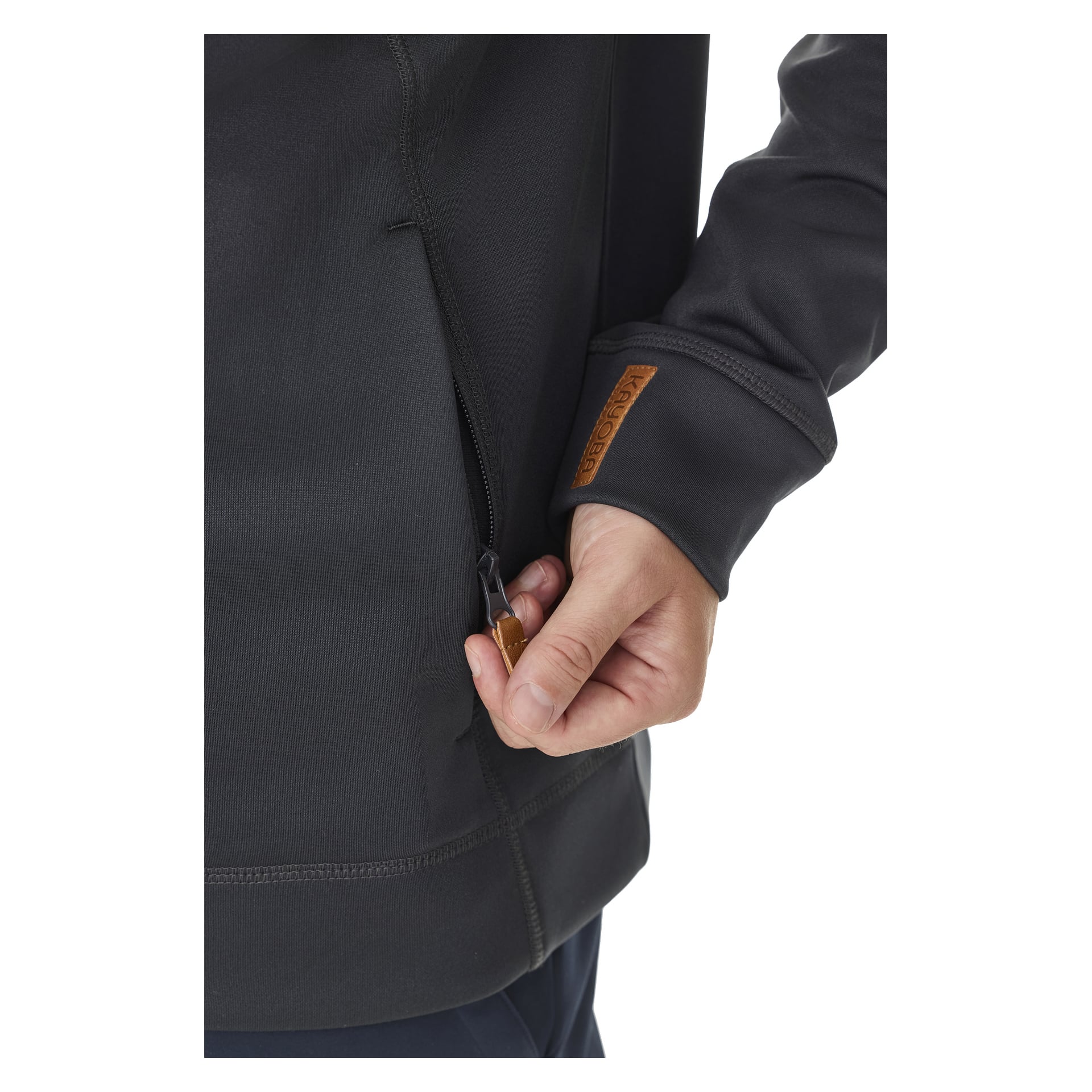 En person som bär Kayoba Outdoor Men's mellanlagertröja Valbo ses dra ner dragkedjan på en sidoficka. Endast deras hand, en del av armen och överkroppen visas. Tröjan har en liten brun lapp med text på ärmen.
