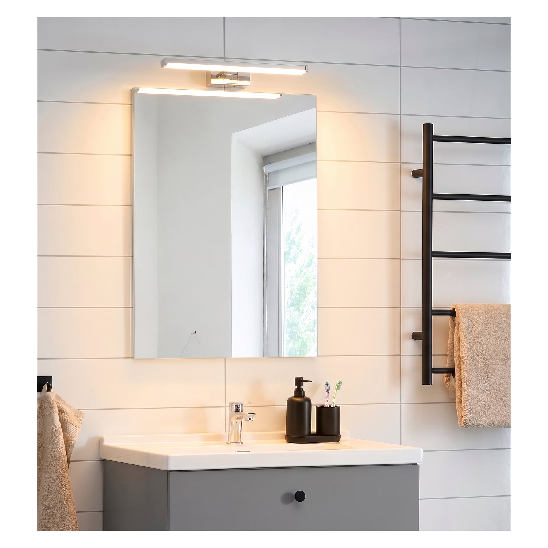 Ett elegant badrum med vita kakelväggar, en rektangulär spegel ovanför handfatet, en horisontellt monterad EKVIP LED-badrumslampa, svarta tvåldispenser på bänken, en handduk hängande på en ställning och ett fönster som släppte in naturligt dagsljus.