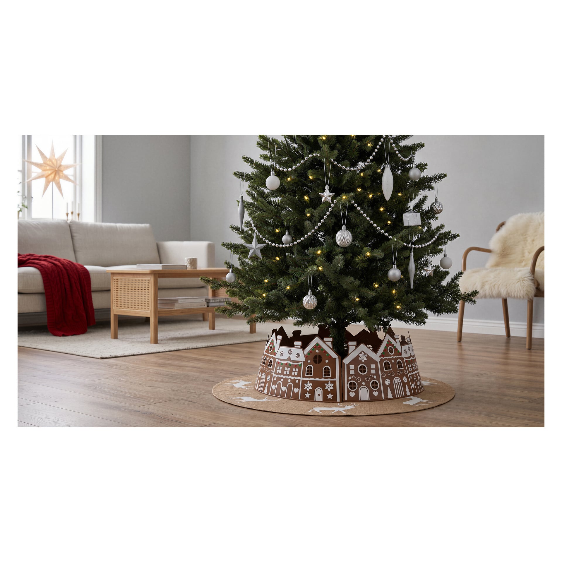 Et festlig pyntet juletre er satt opp i en stue, pakket inn i bunnen med EKVIPs juletrekrage som viser et herlig pepperkakehusmotiv. Treet er dekorert med hvite og sølvfargede ornamenter og opplyst med lysslynger, mens en beige sofa og et salongbord i tre er synlig i bakgrunnen.