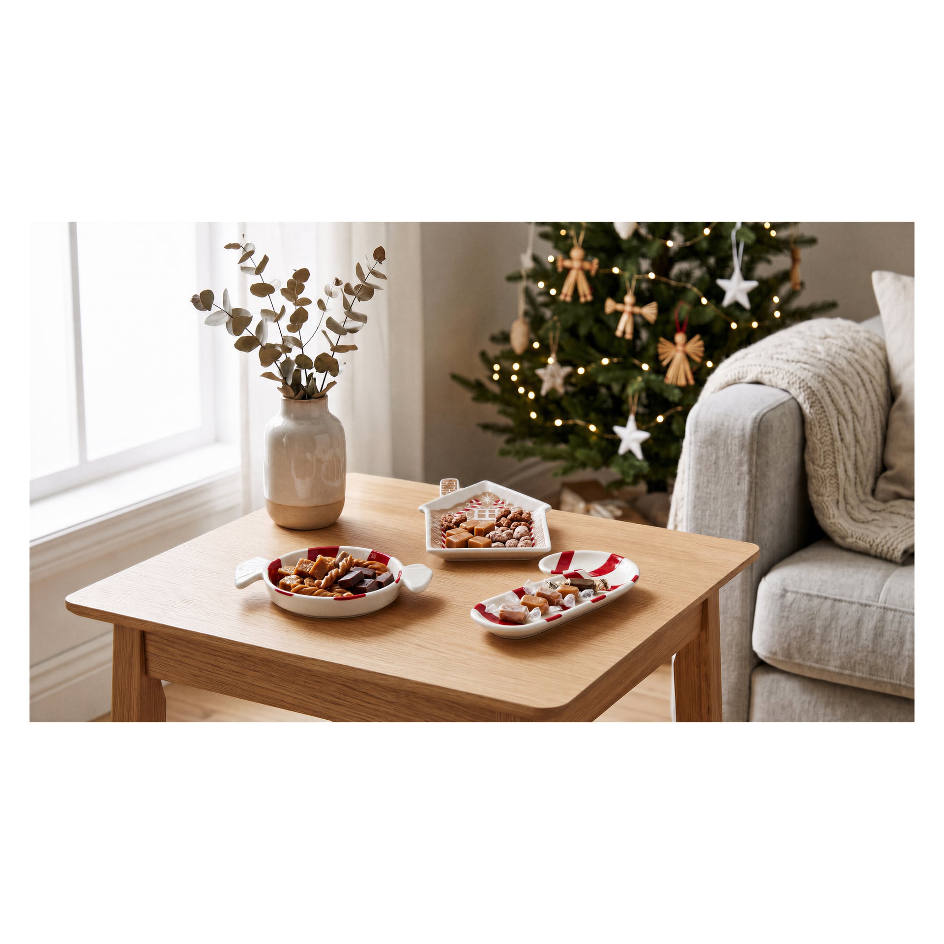 En festlig tallrik med en polkagris från EKVIP står på ett träbord, placerad framför en soffa och en julgran prydd med dekorationer. I närheten står en vas fylld med torkade grenar bredvid ett solbelyst fönster.