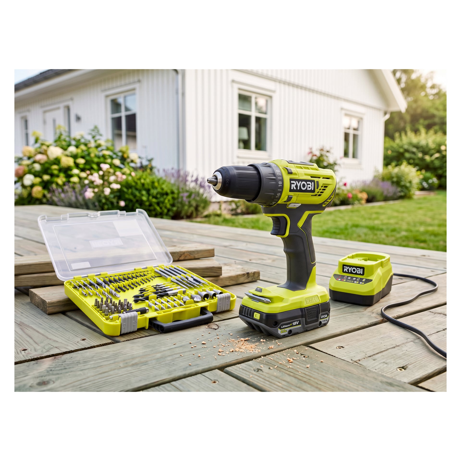 Ryobi One+ -porakone, terät ja akku (R18DD32-1C20GA60J) istuu puisella ulkopöydällä, jonka takana näkyy talo ja puutarha.