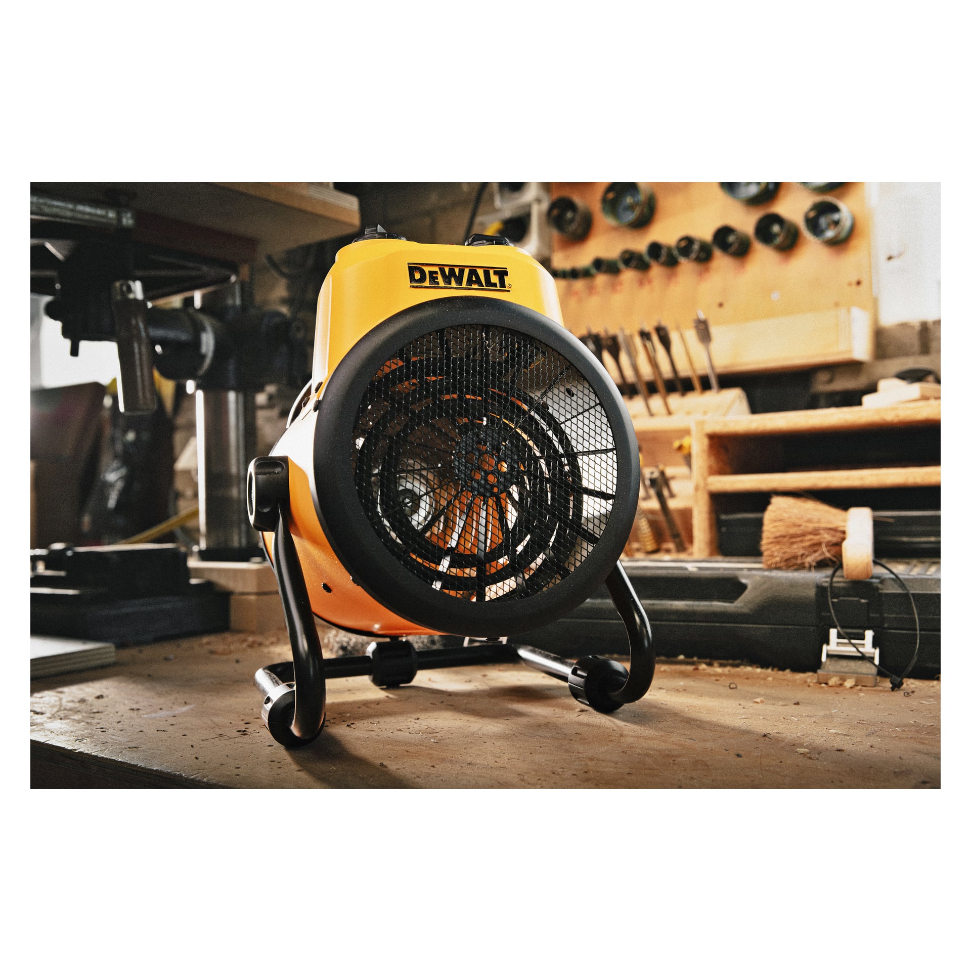 En DeWalt Heater Fan DXJHXA0002E står på en arbetsbänk inne i en verkstad, omgiven av olika verktyg och utrustning i bakgrunden.