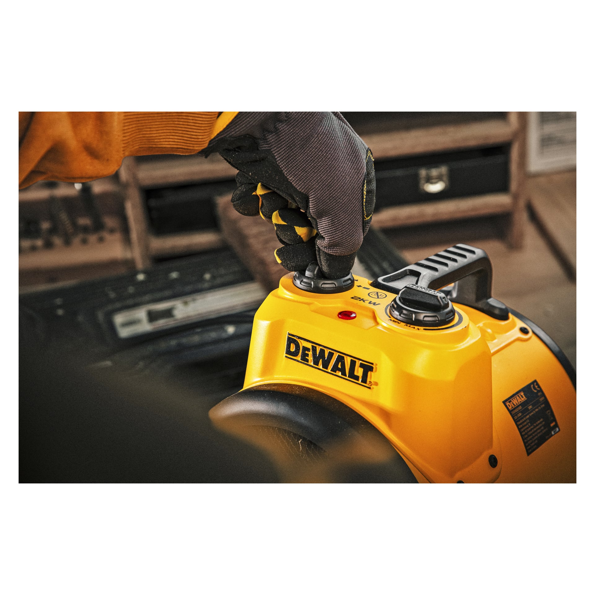 En handskbeklädd hand vrider på en ratt på en gul DeWalt Heater Heater fläkt DXJHXA0002E, med dess märkta kontrollpanel och handtag synliga.